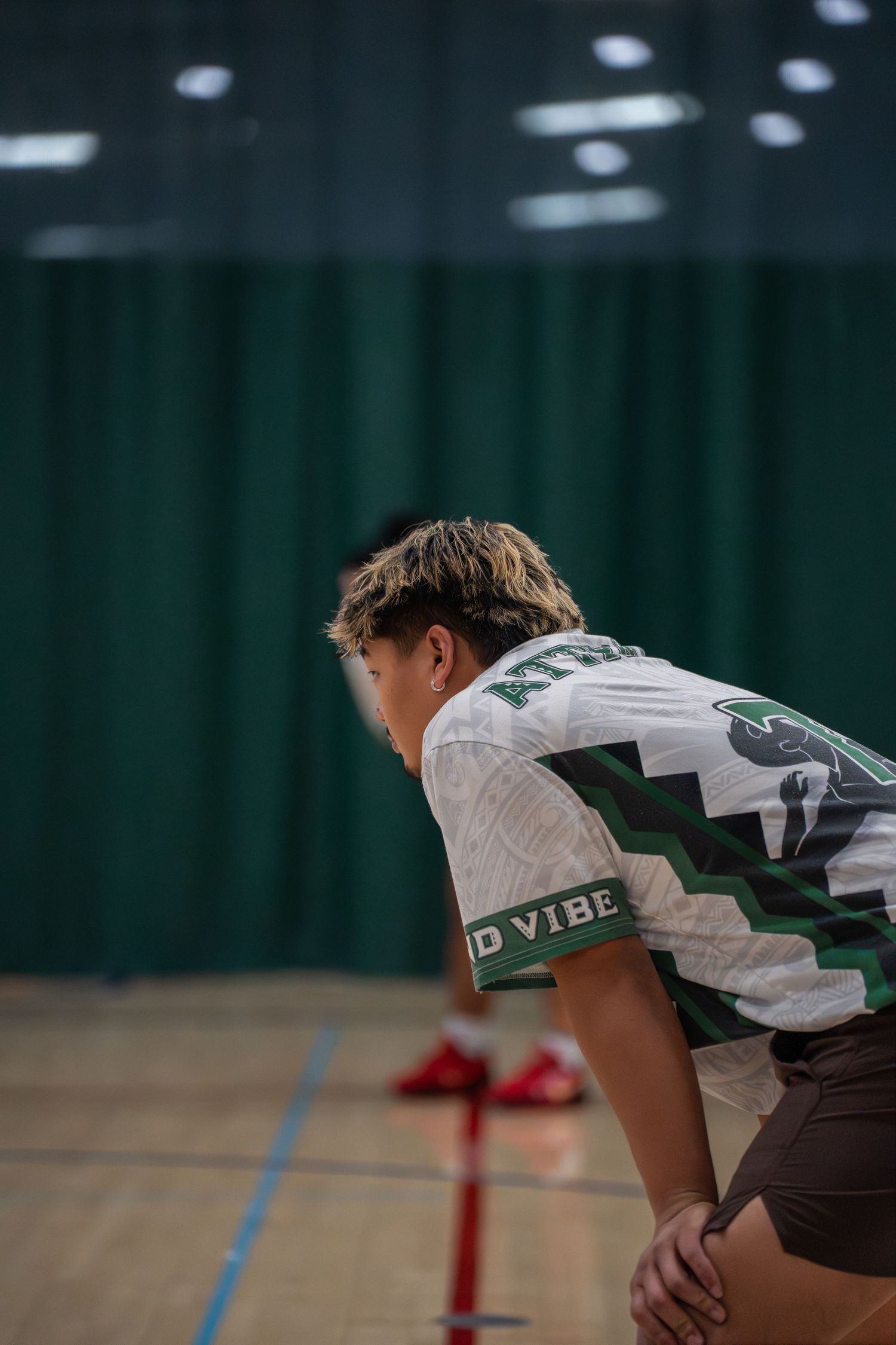 Football player in white jersey crouches down on indoor sports field.