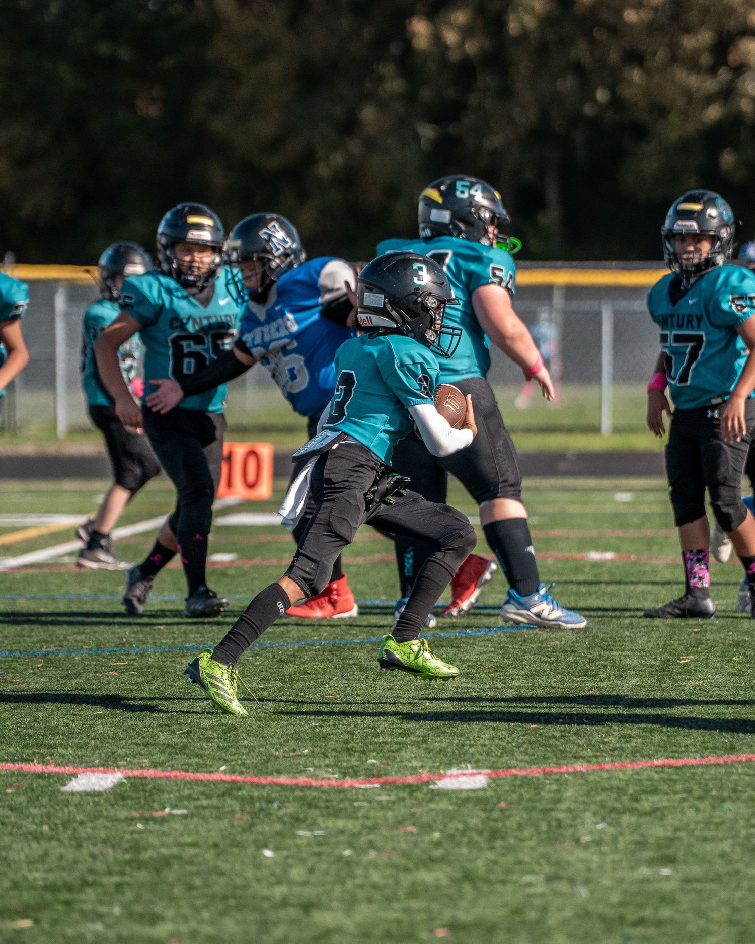 Football players in teal and black uniforms practice on artificial turf field.