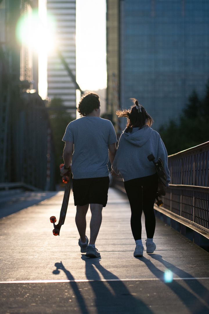 Silhouettes of people walking with skateboards on urban bridge at dusk.