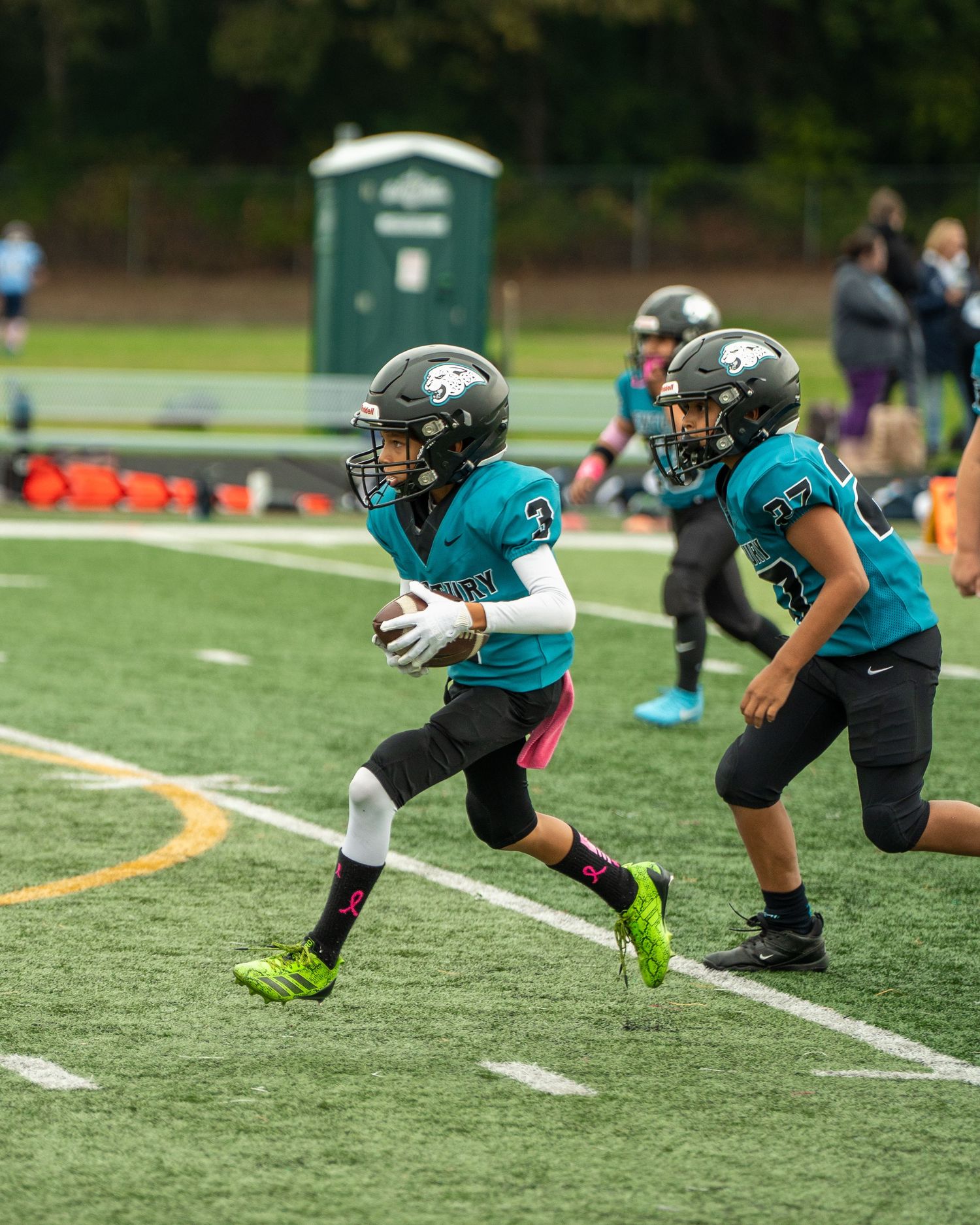 Players in teal uniforms perform synchronized running drills on football field.