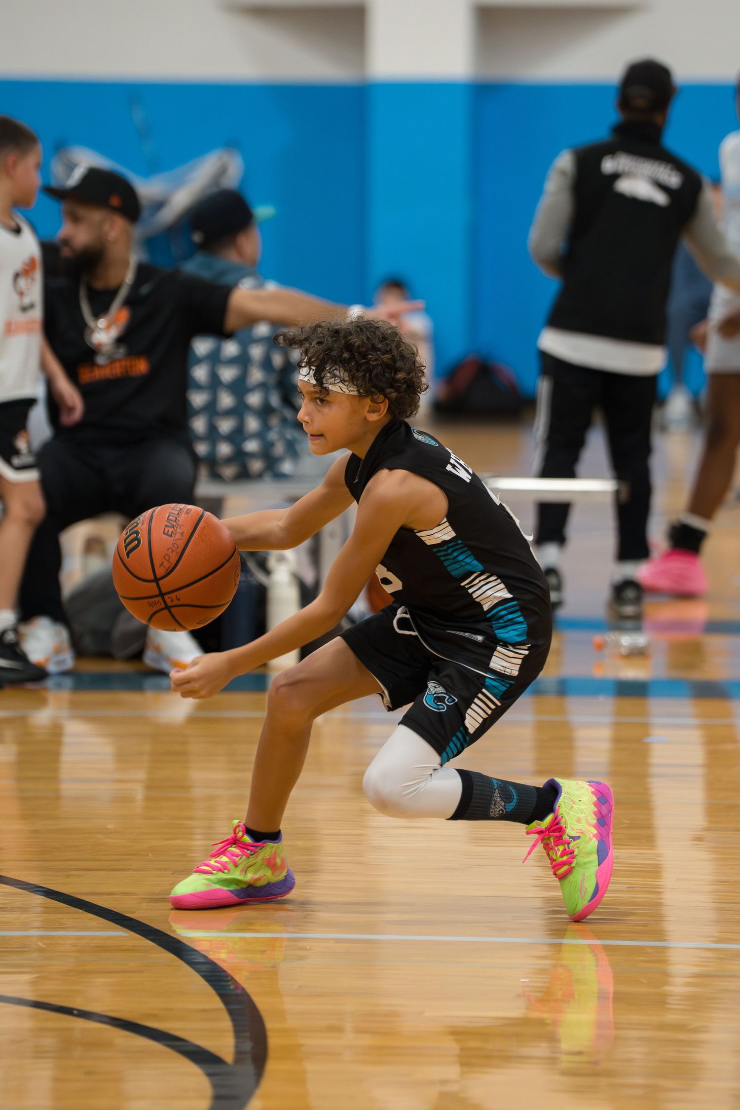 Basketball player in black uniform performs dribbling drill sequence on wooden court with pink shoes.