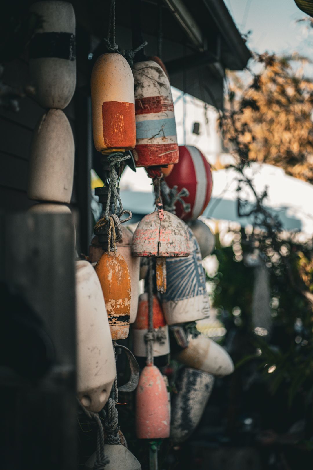 Collection of weathered buoys hanging from building eave in various faded colors.