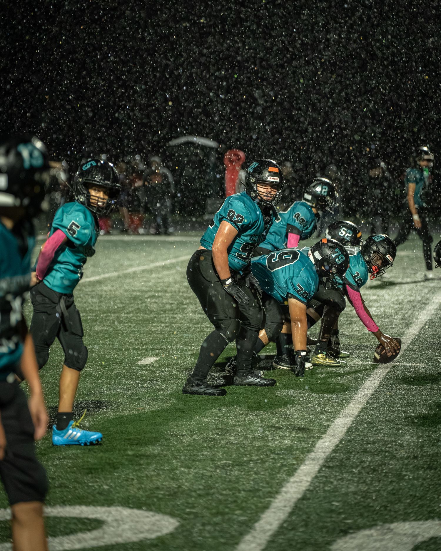 Football team in teal uniforms lines up in formation during a snowy night game.