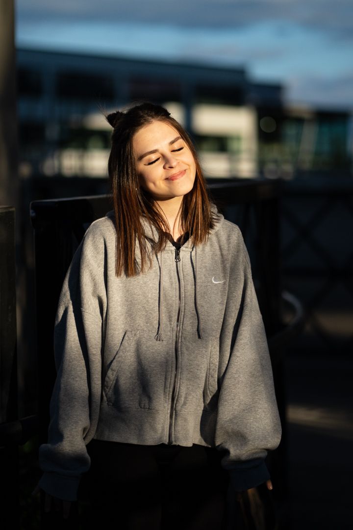 Person in grey hoodie basking in sunset light with eyes closed.
