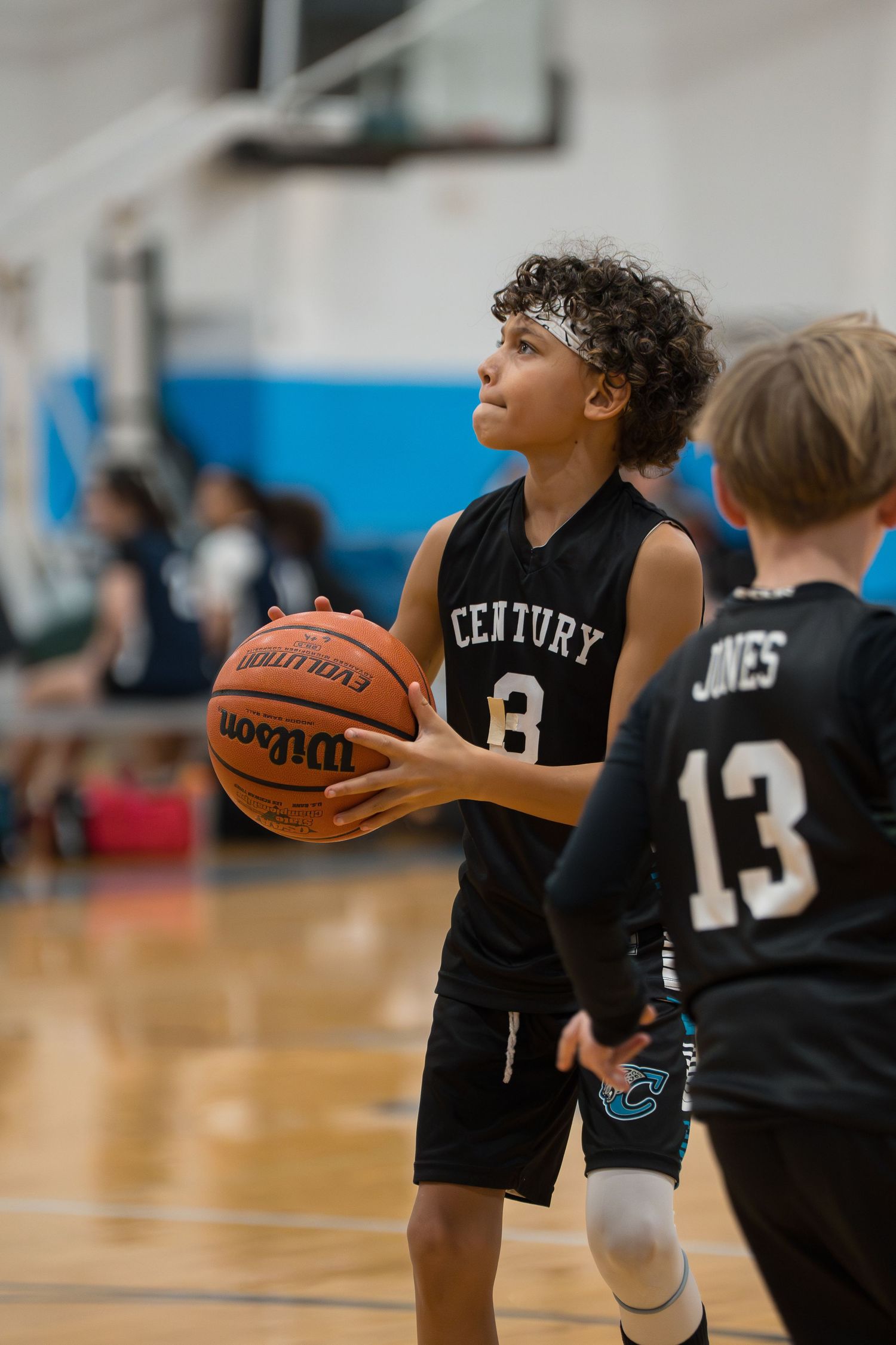 Young basketball players in black jerseys practice shooting drills during a youth sports training session in a gymnasium.