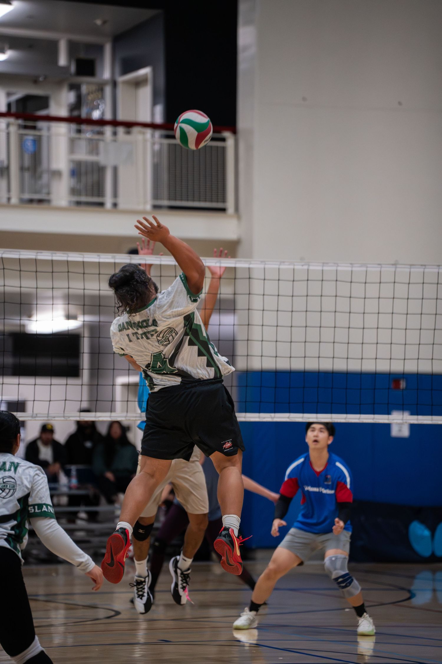 Athletes diving and reaching for a volleyball during an indoor match.