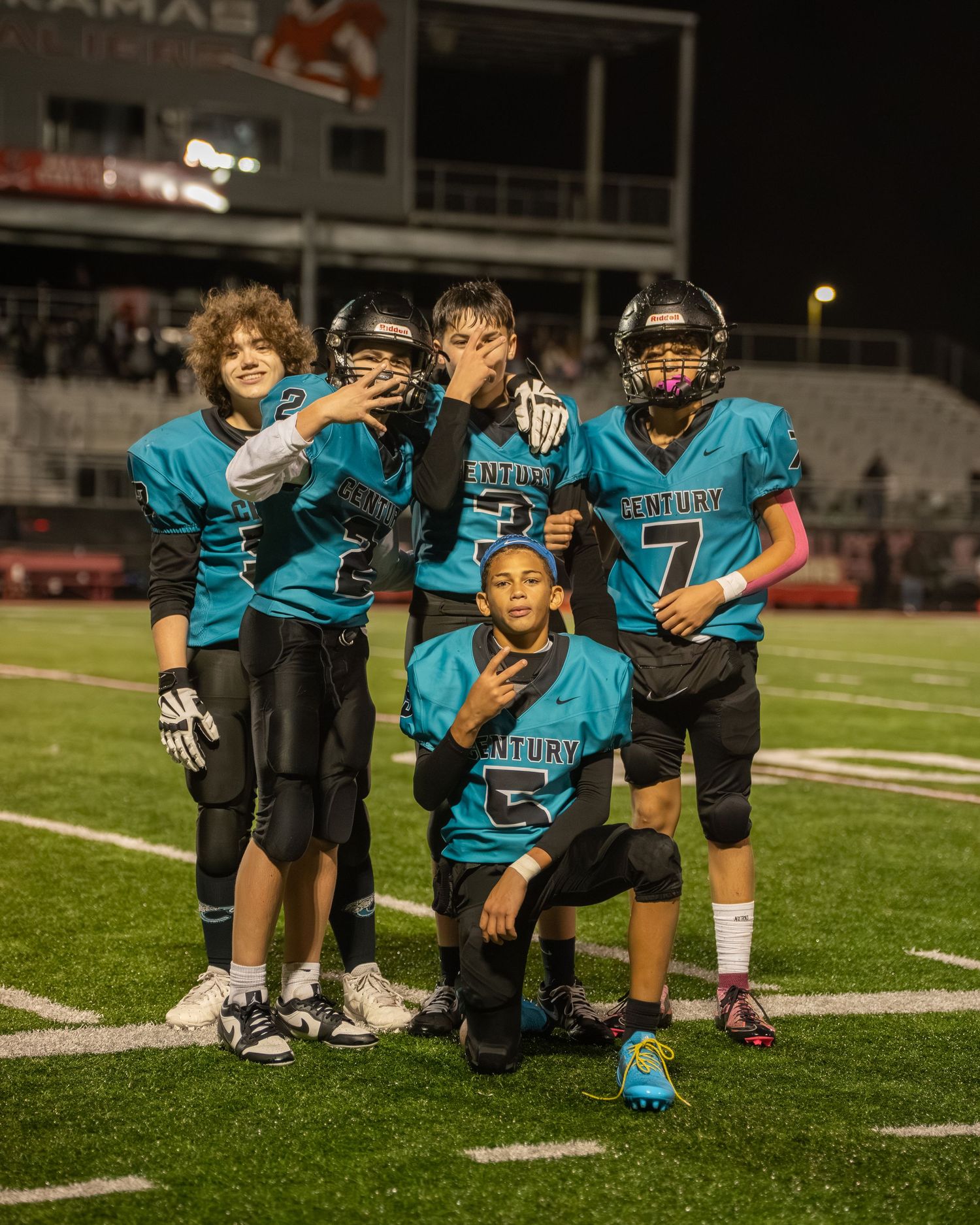 Youth football team in teal uniforms kneels together on the field during practice.