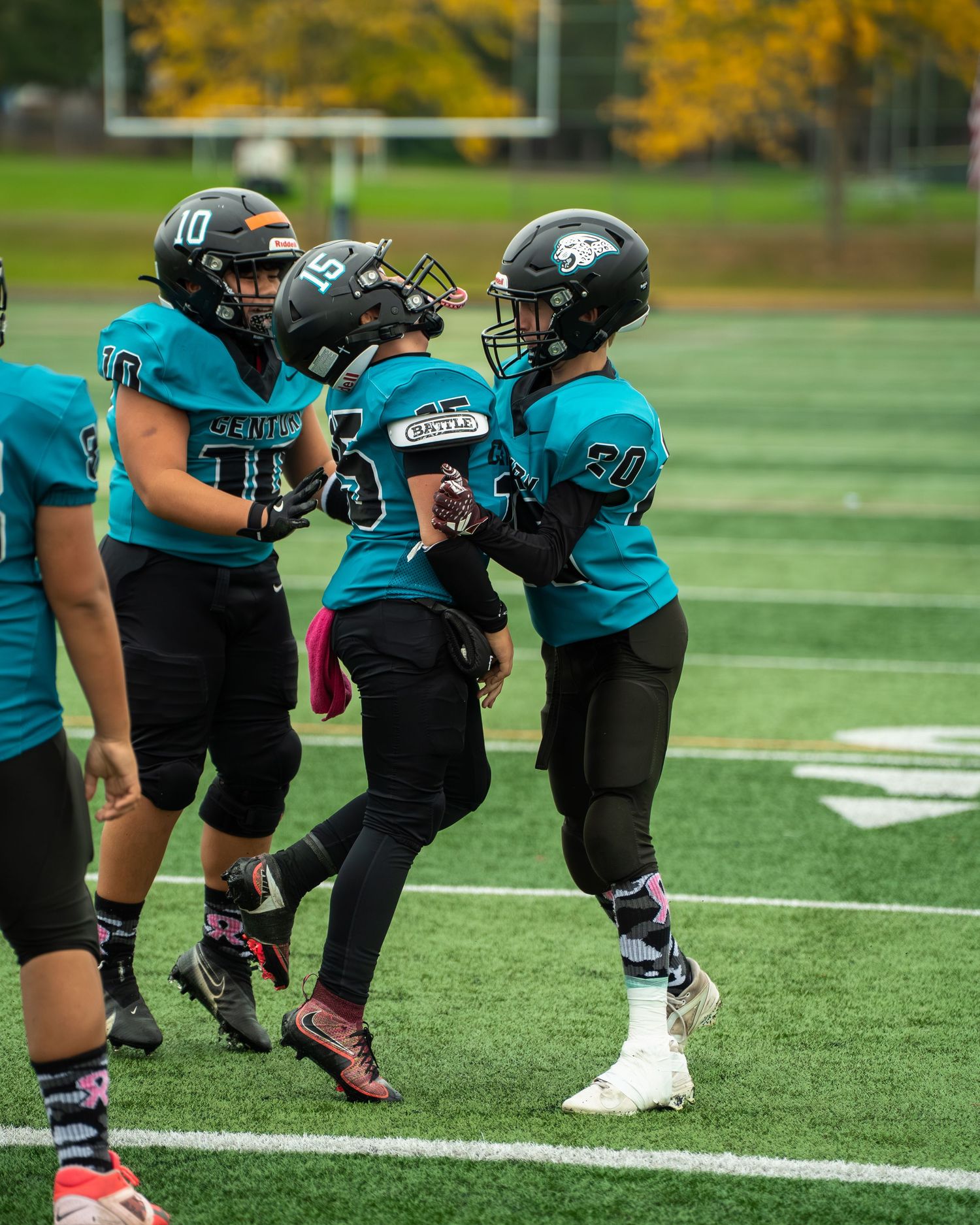 Three football players in teal uniforms celebrate together on the field.