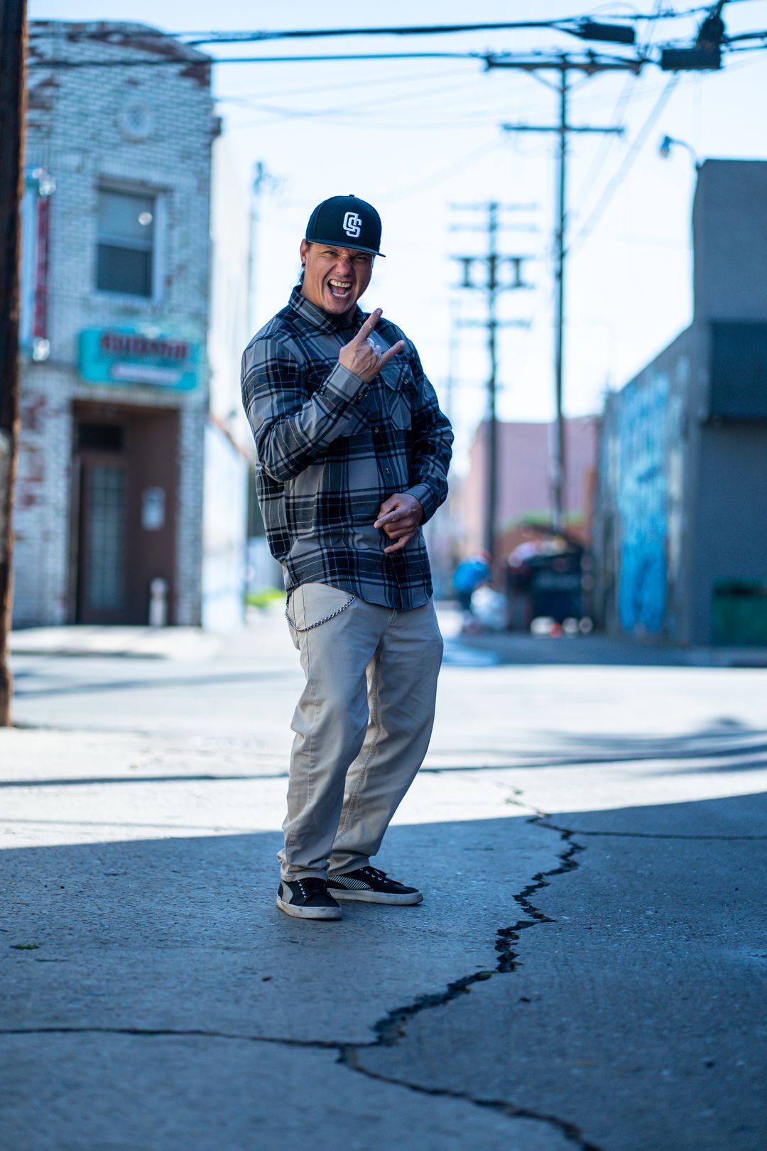 Figure in plaid jacket and baseball cap standing on a quiet urban street.