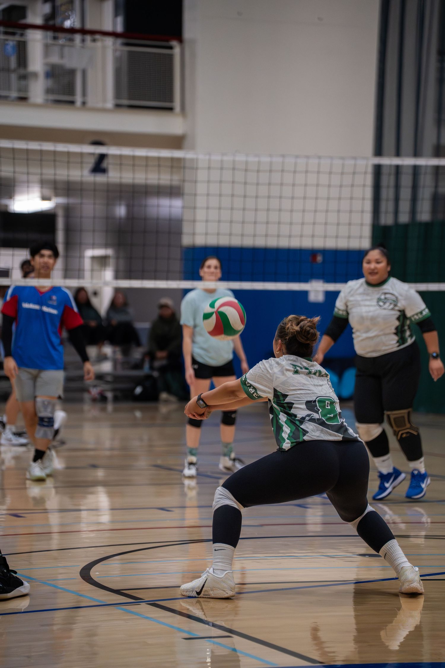 Indoor volleyball players in action showing defensive positions on the court during a game.