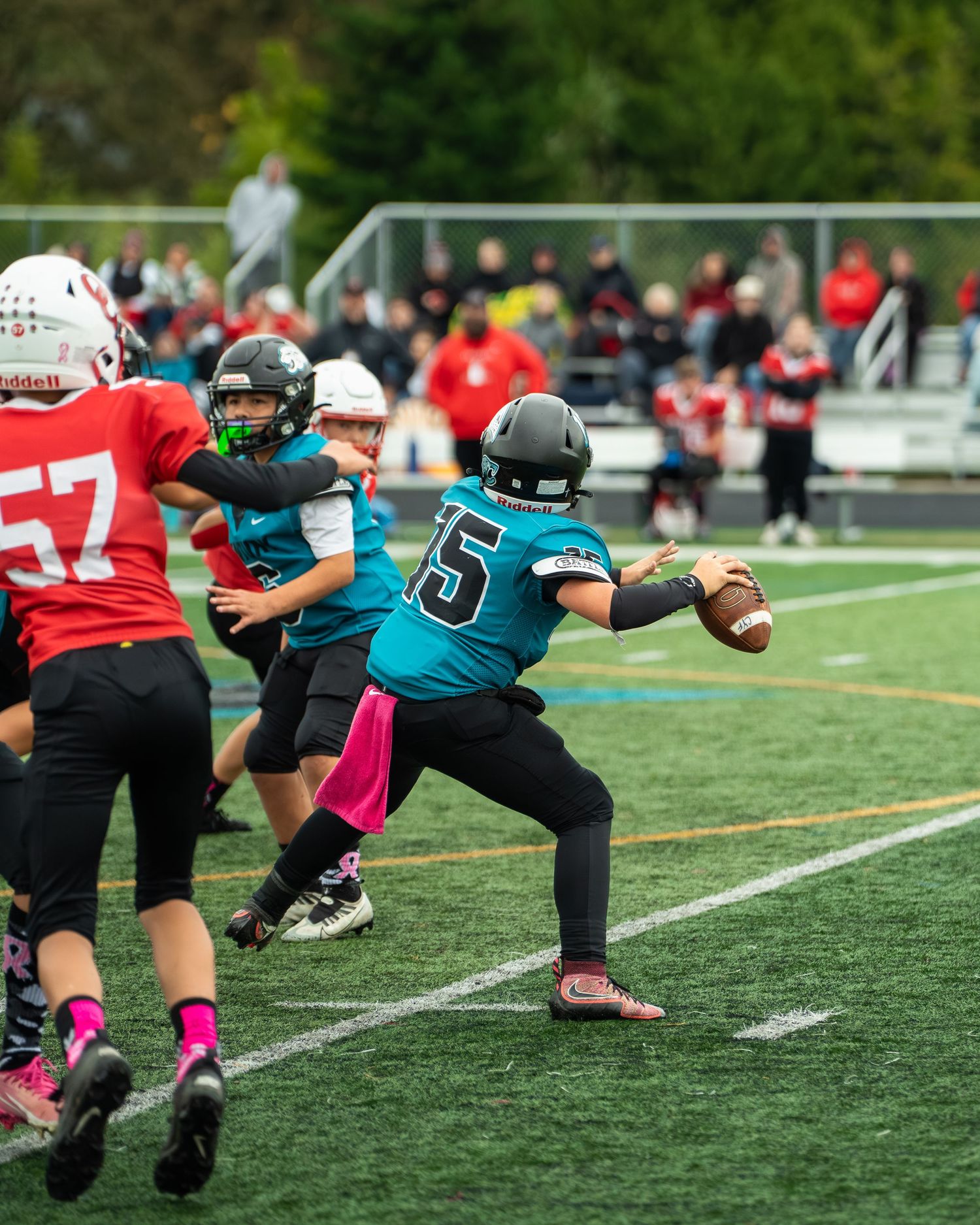 A football player in teal uniform prepares to throw while teammates block defenders.