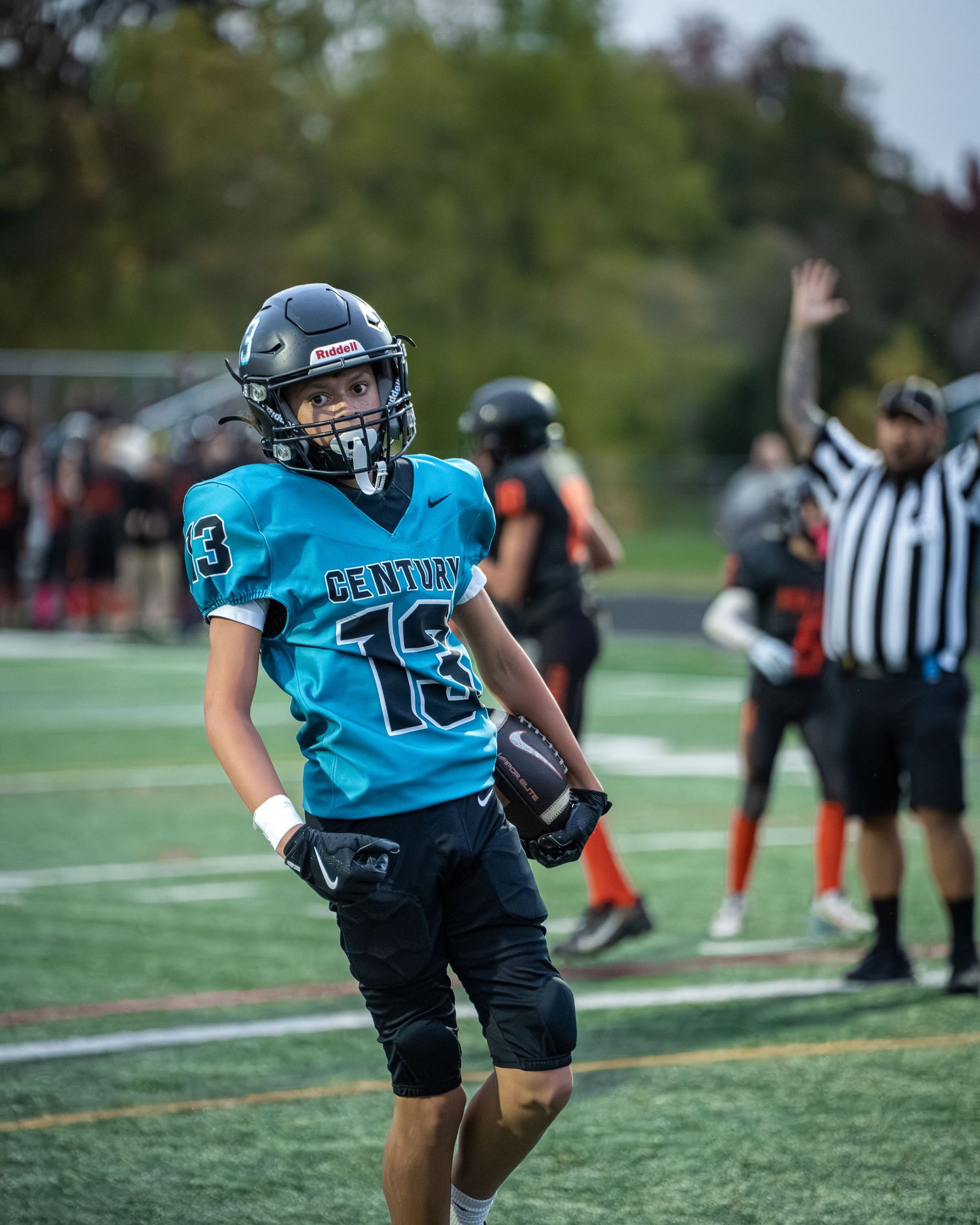 Youth football player in teal jersey runs with the ball during practice on artificial turf field.
