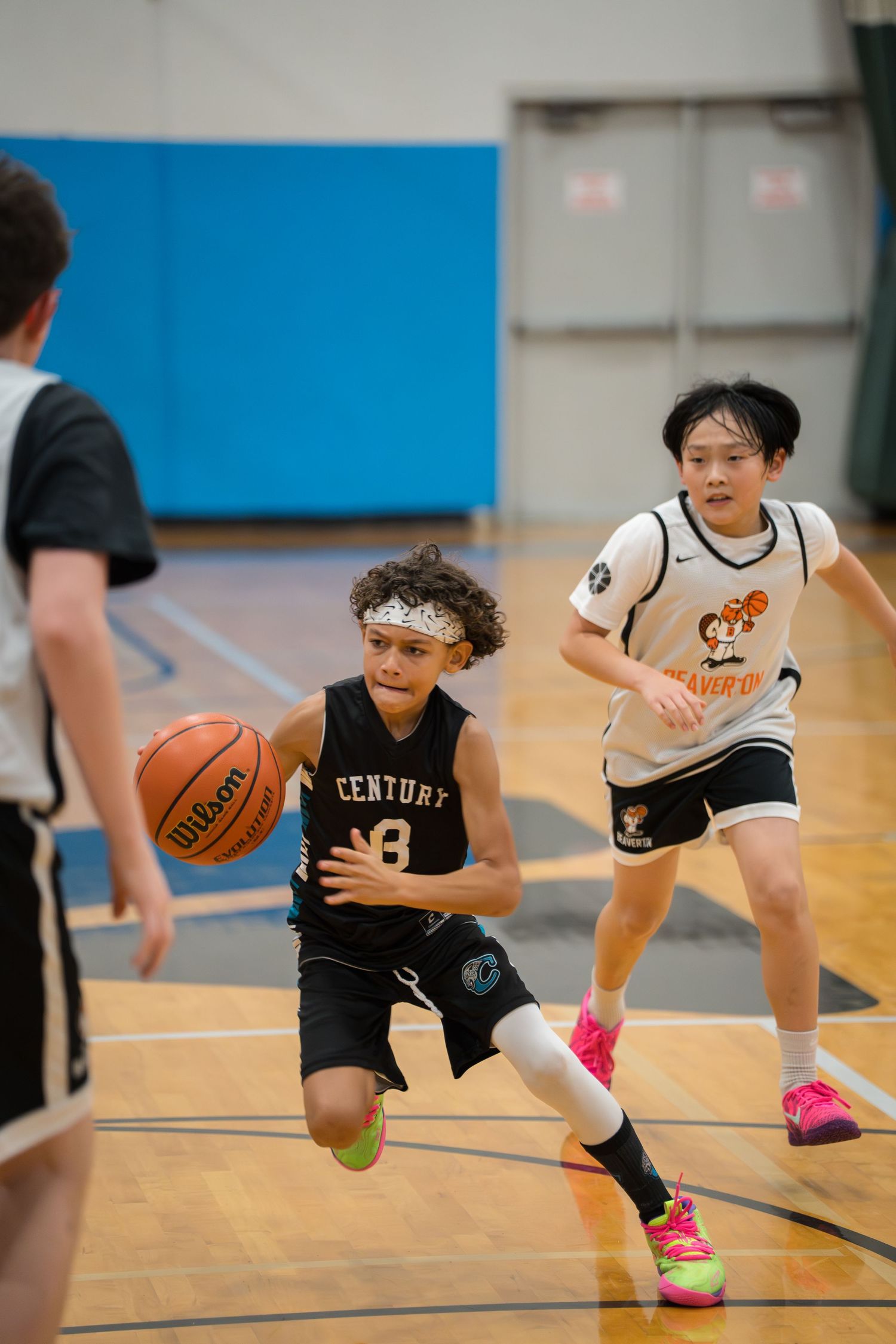 Youth basketball players in black and white jerseys practice dribbling drills on an indoor court during training.