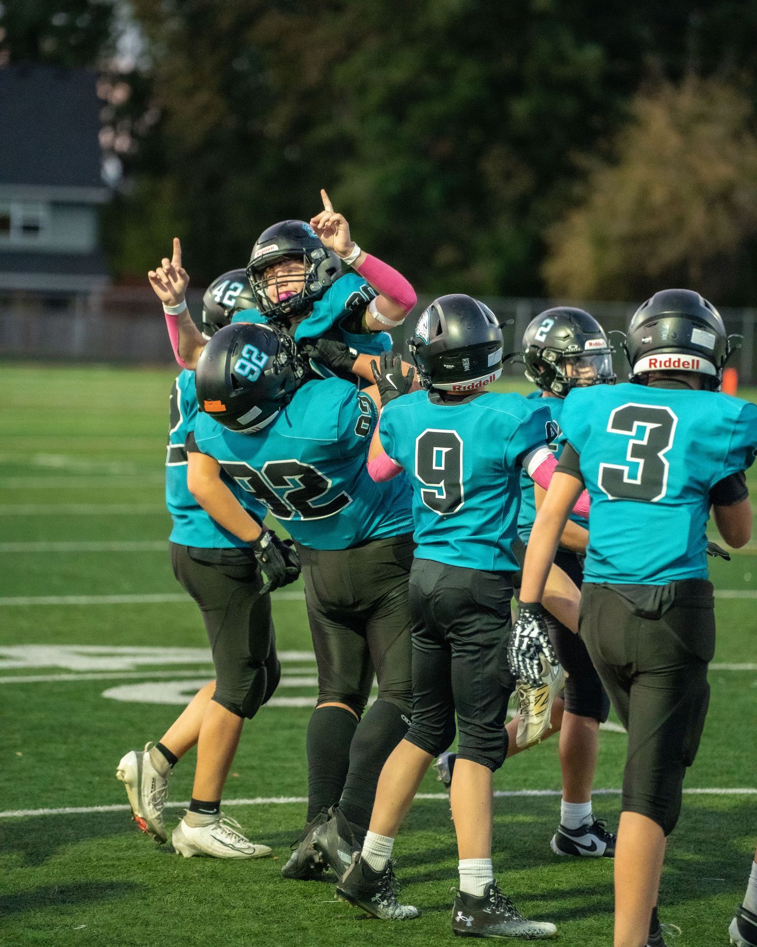 Football team in teal uniforms lines up in formation on the field.