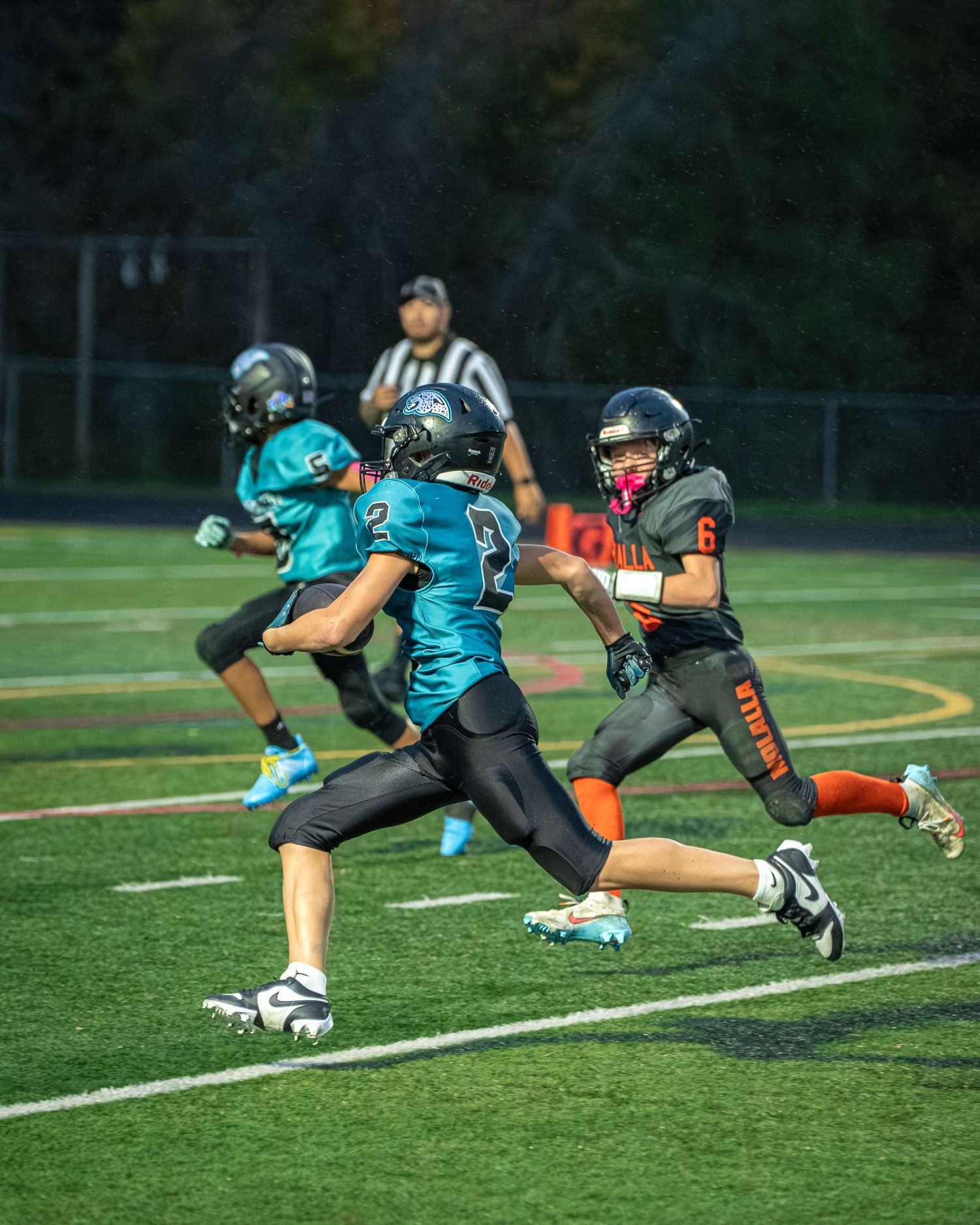 Football players diving and practicing defensive maneuvers on an illuminated field at dusk.