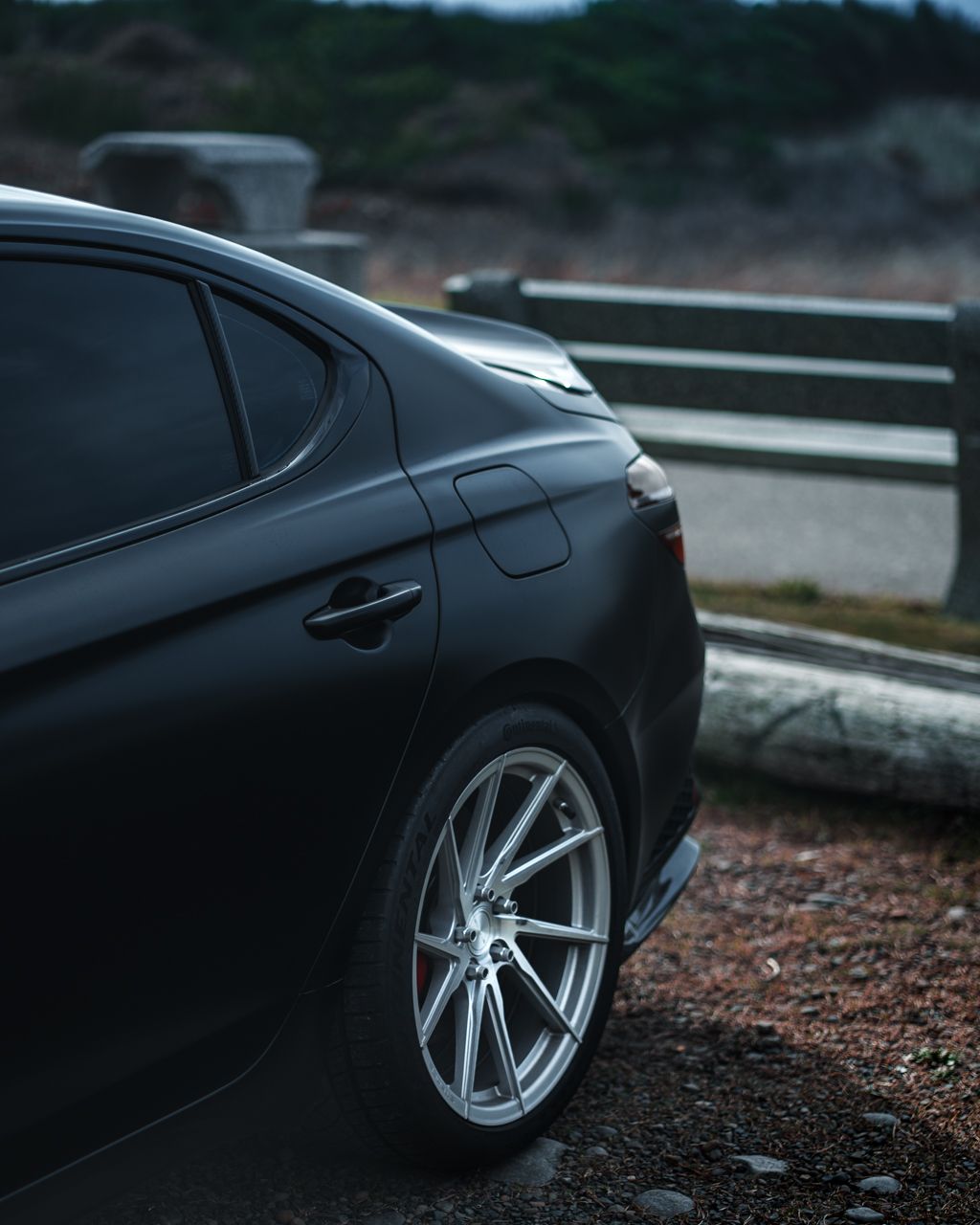 Side profile view of a black luxury sports car with custom silver wheels against a dark background.