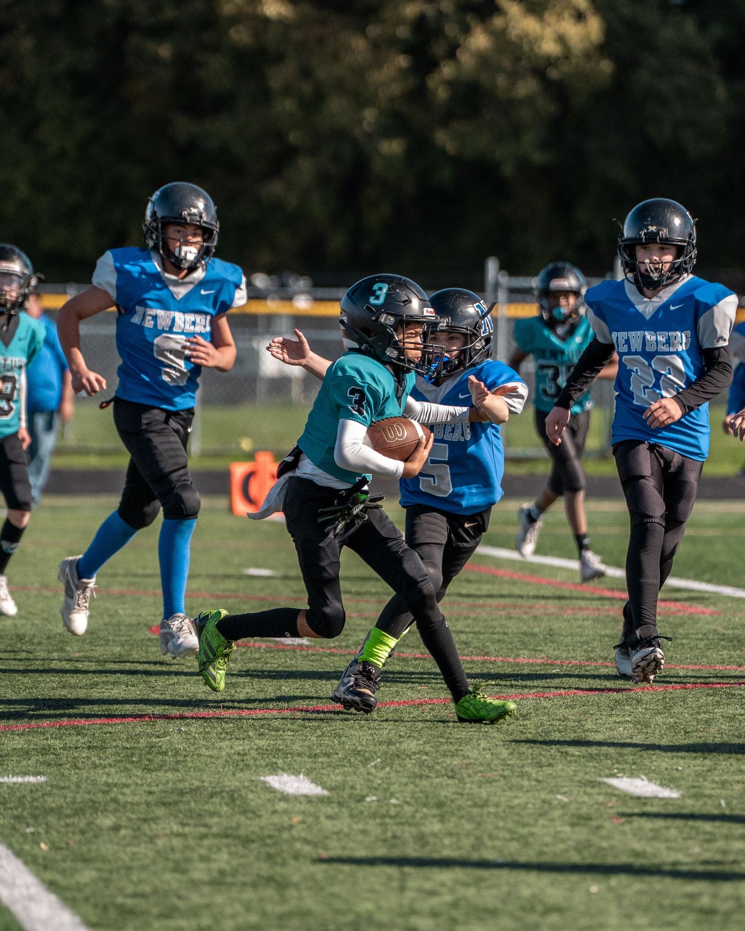 Youth football players in teal and blue uniforms practice diving techniques on field.