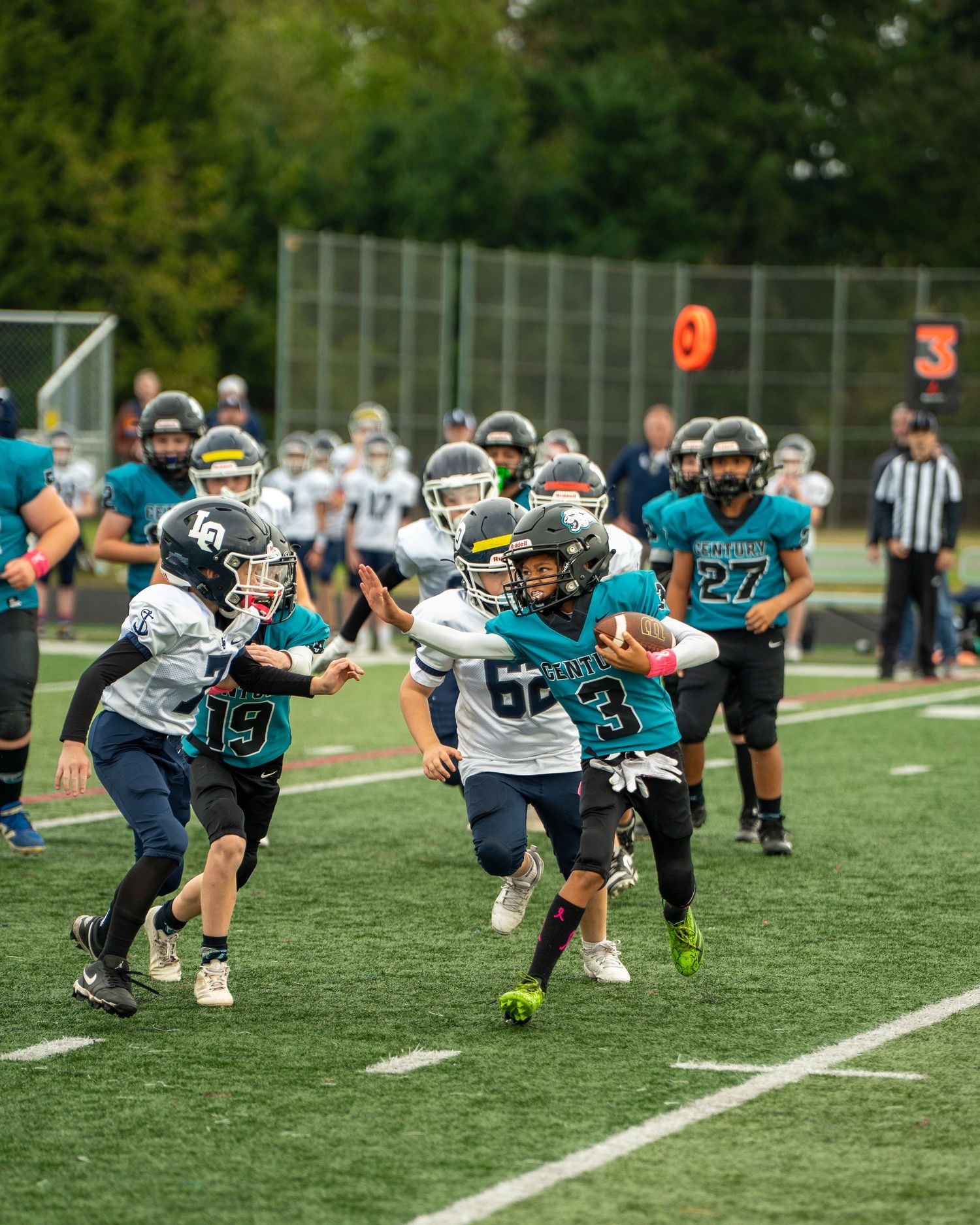 Youth football players from opposing teams engage in a play on the field.