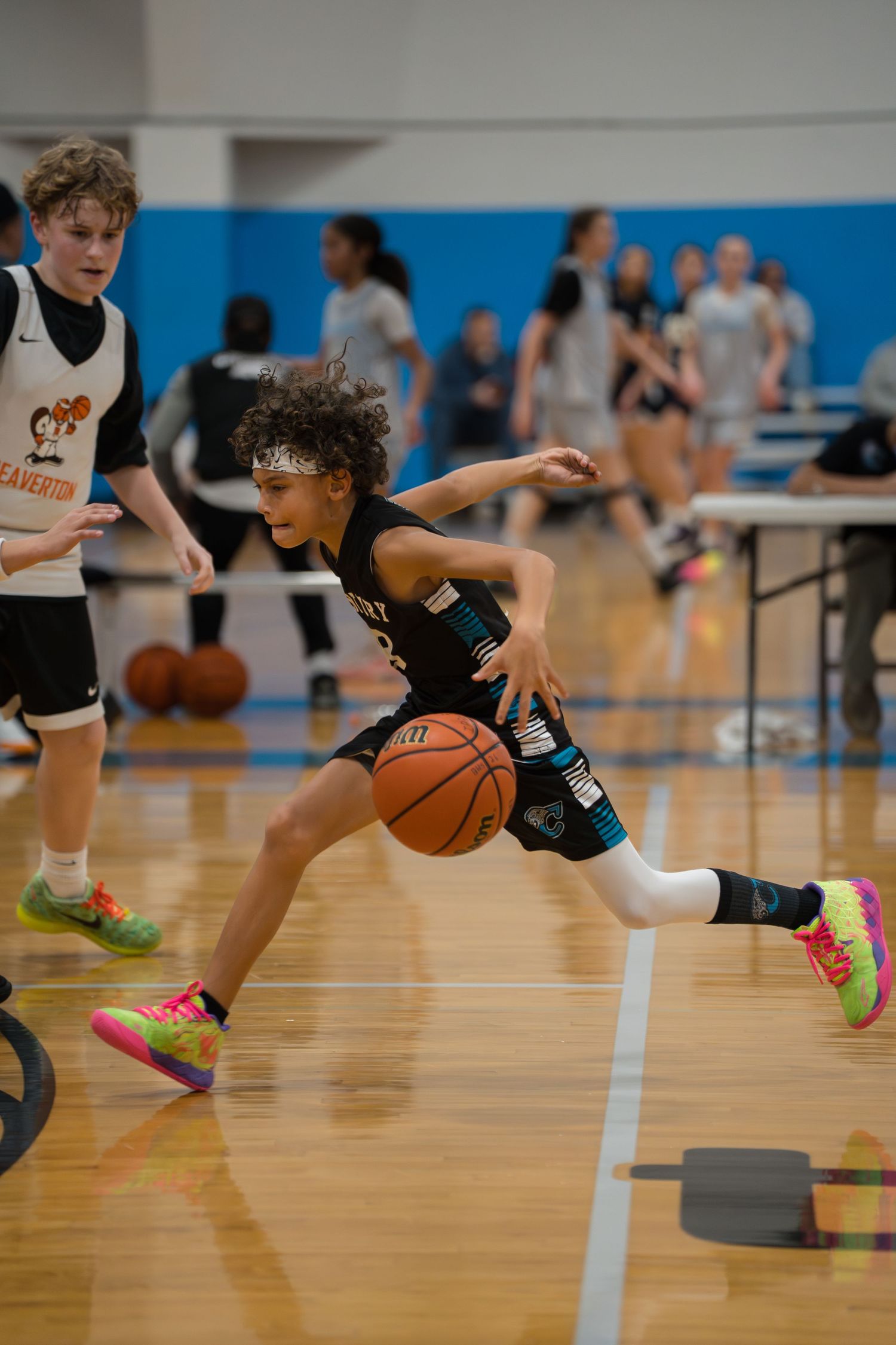 Youth basketball players practice dribbling drills around cones on a wooden gymnasium floor during training.