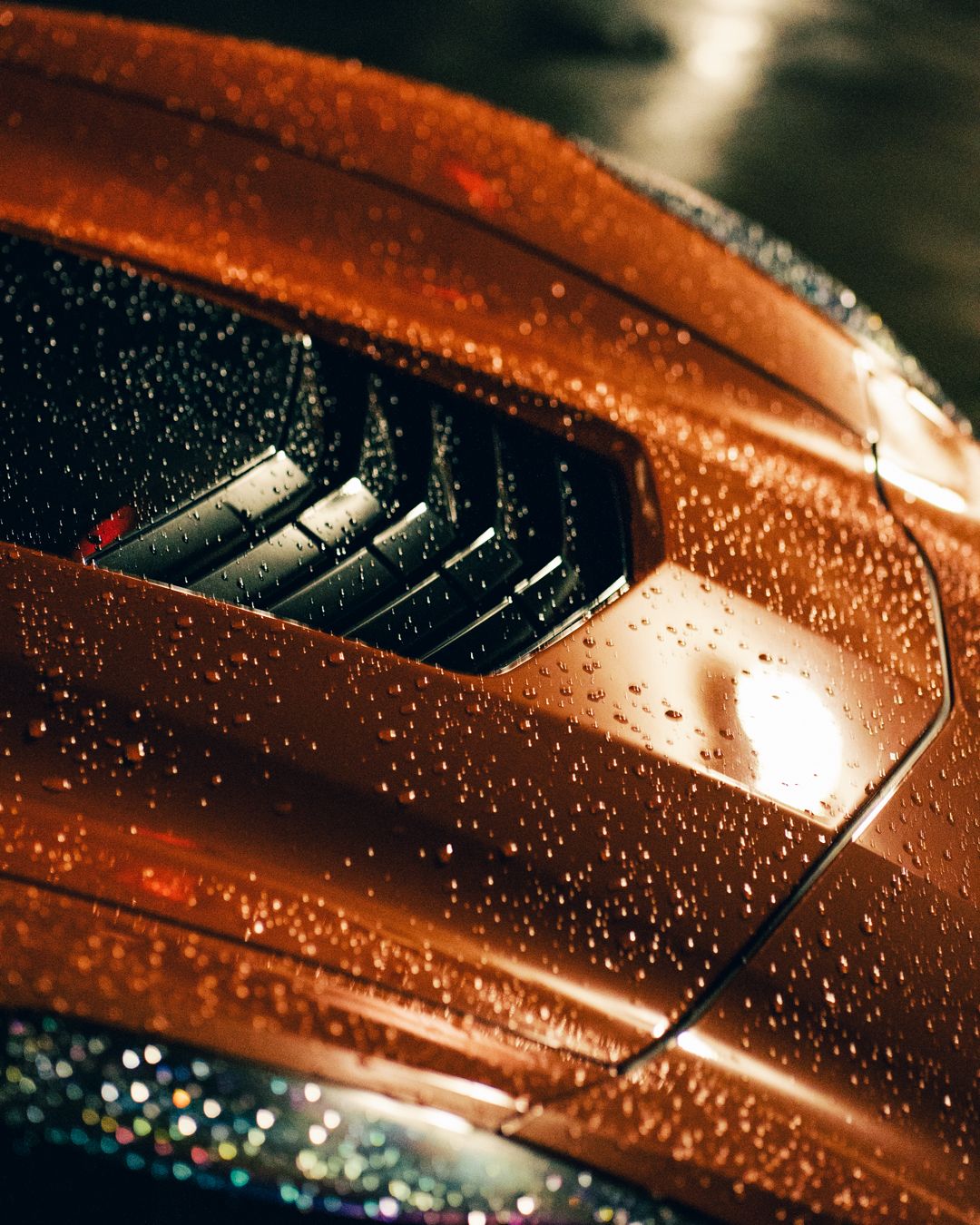 Macro shot of water droplets on orange Corvette's ventilated hood panel.