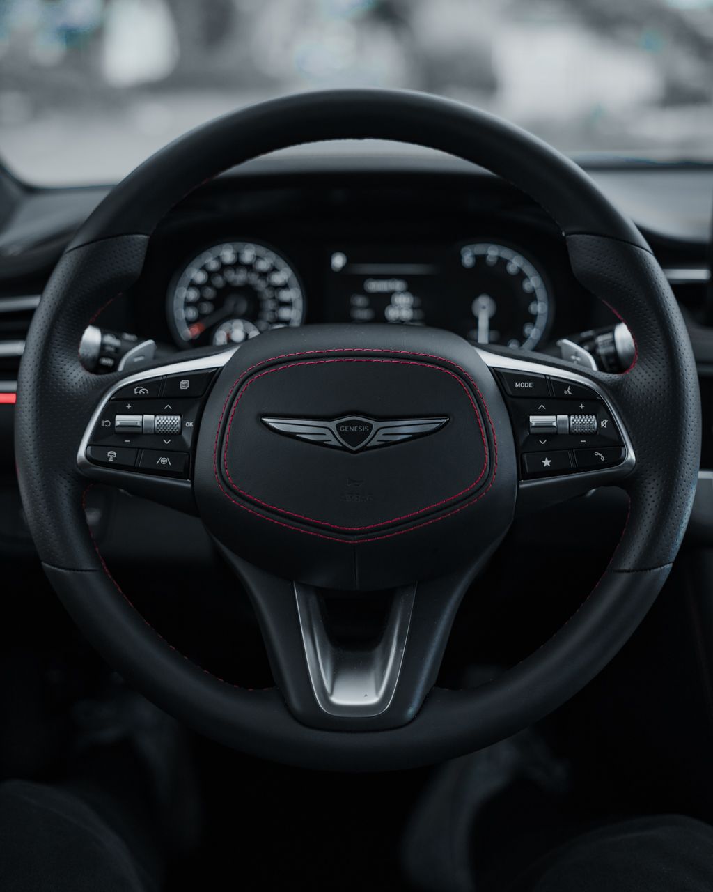 Modern steering wheel design with black leather and red accent stitching in luxury vehicle.
