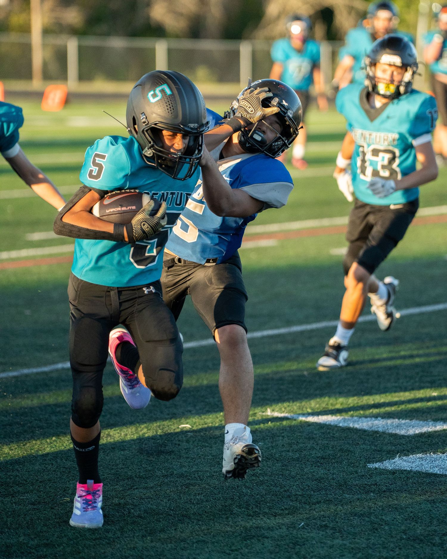 Youth football players in teal jerseys running drills on sports field.