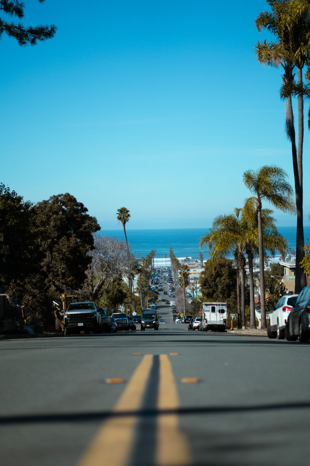 Steep residential street with palm trees leading to ocean view in California.