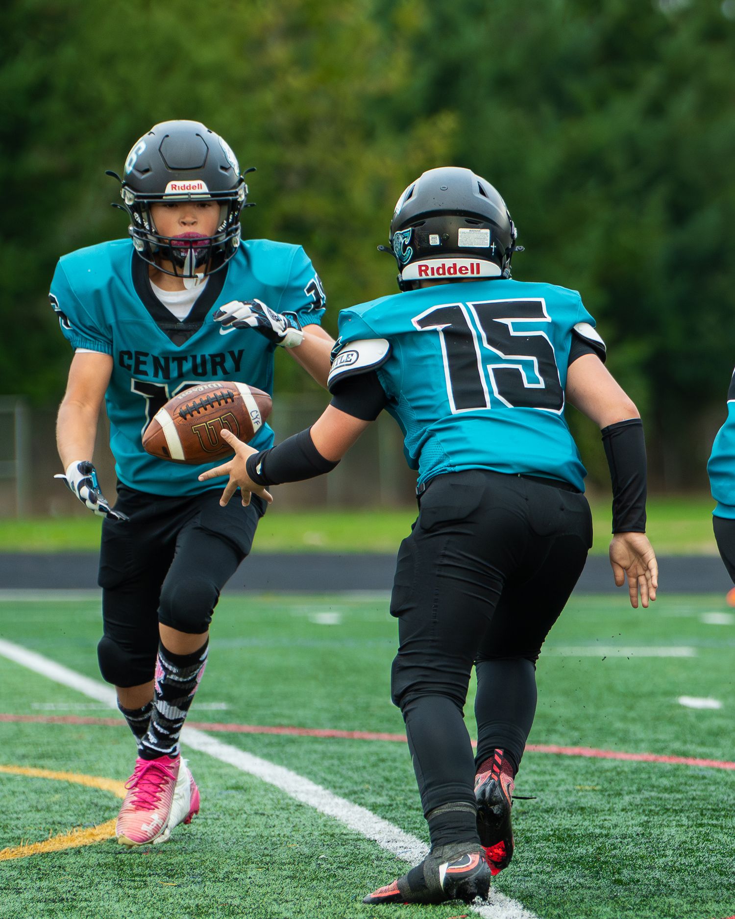 Players in teal jerseys practice running drills on football field with pink cleats.