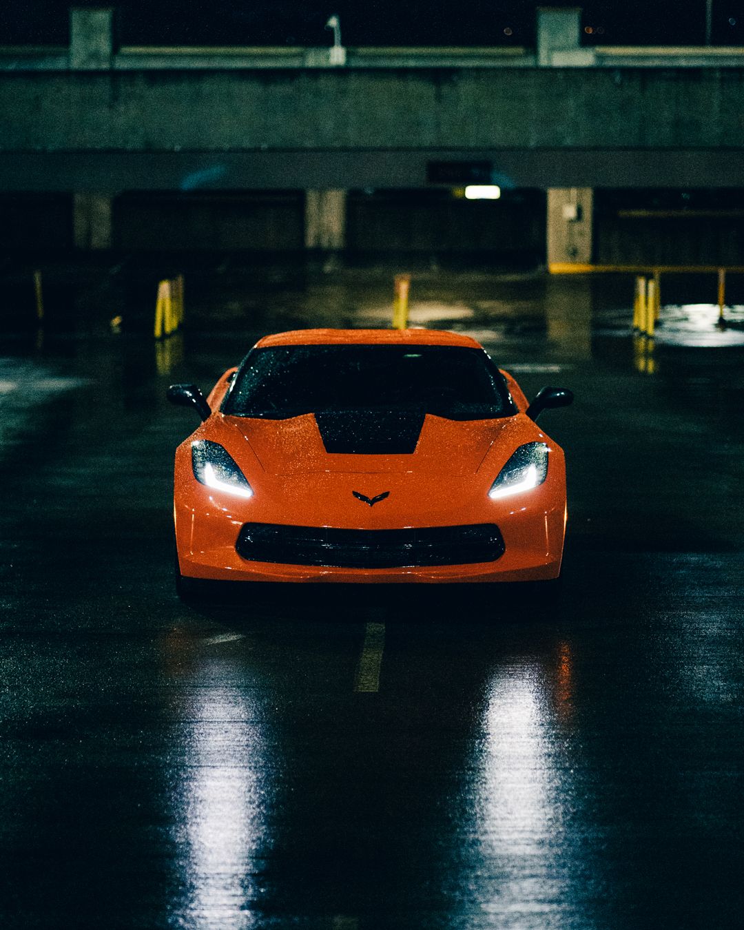 Orange Corvette sports car with glowing headlights in dark parking garage.