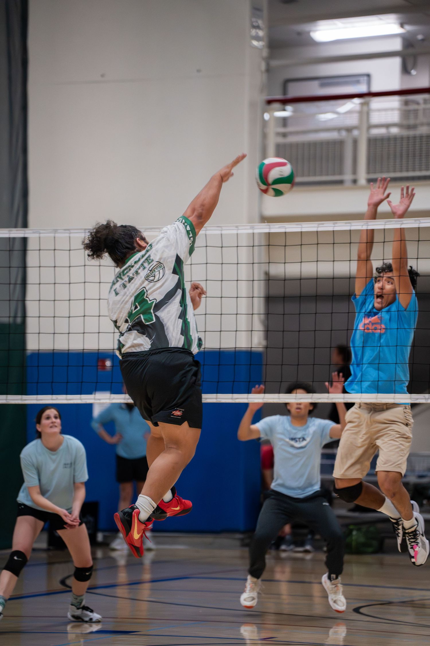 Players leaping and reaching for the volleyball during an intense indoor match.
