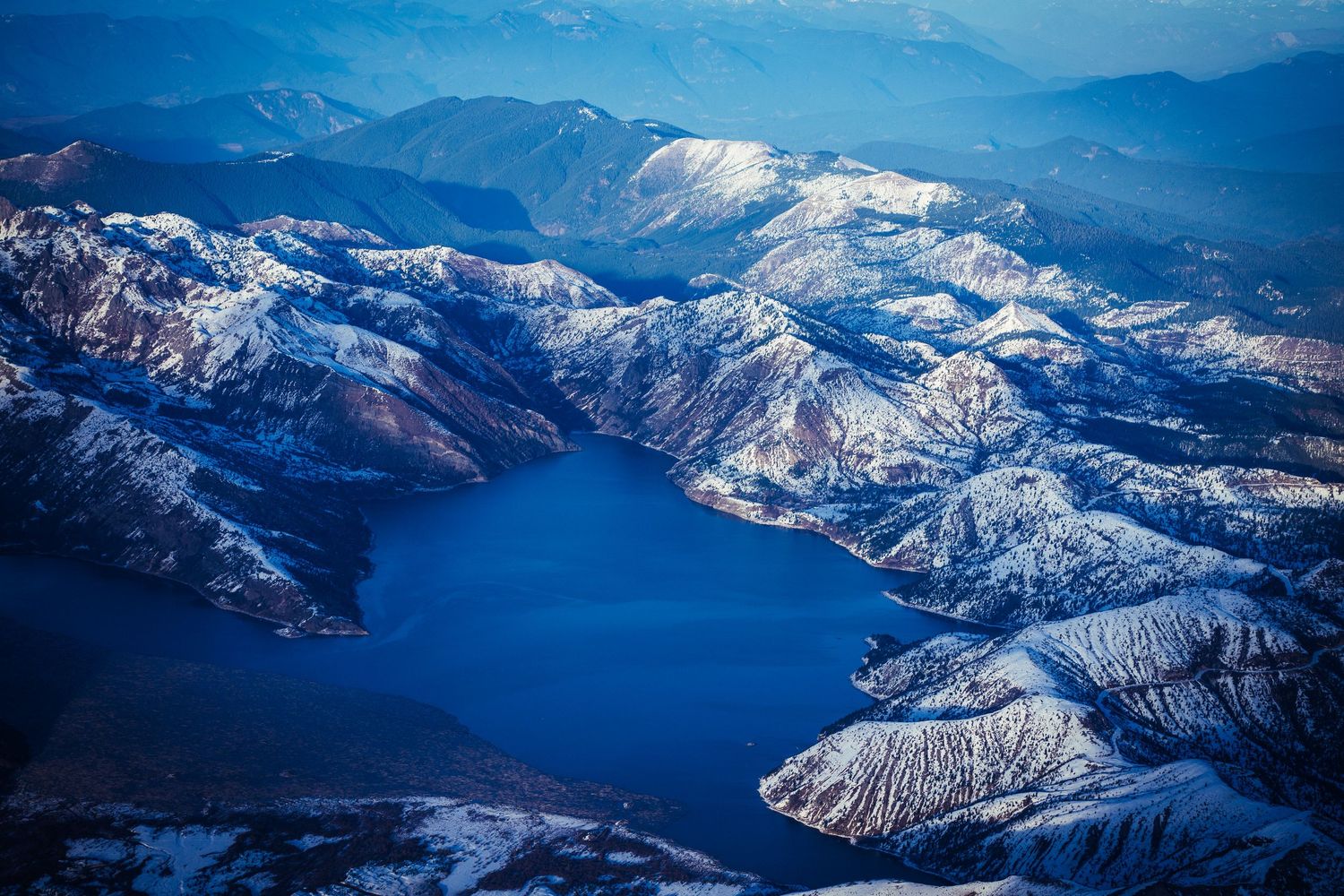 Aerial view of snow-capped mountains and lakes under a bright blue sky.