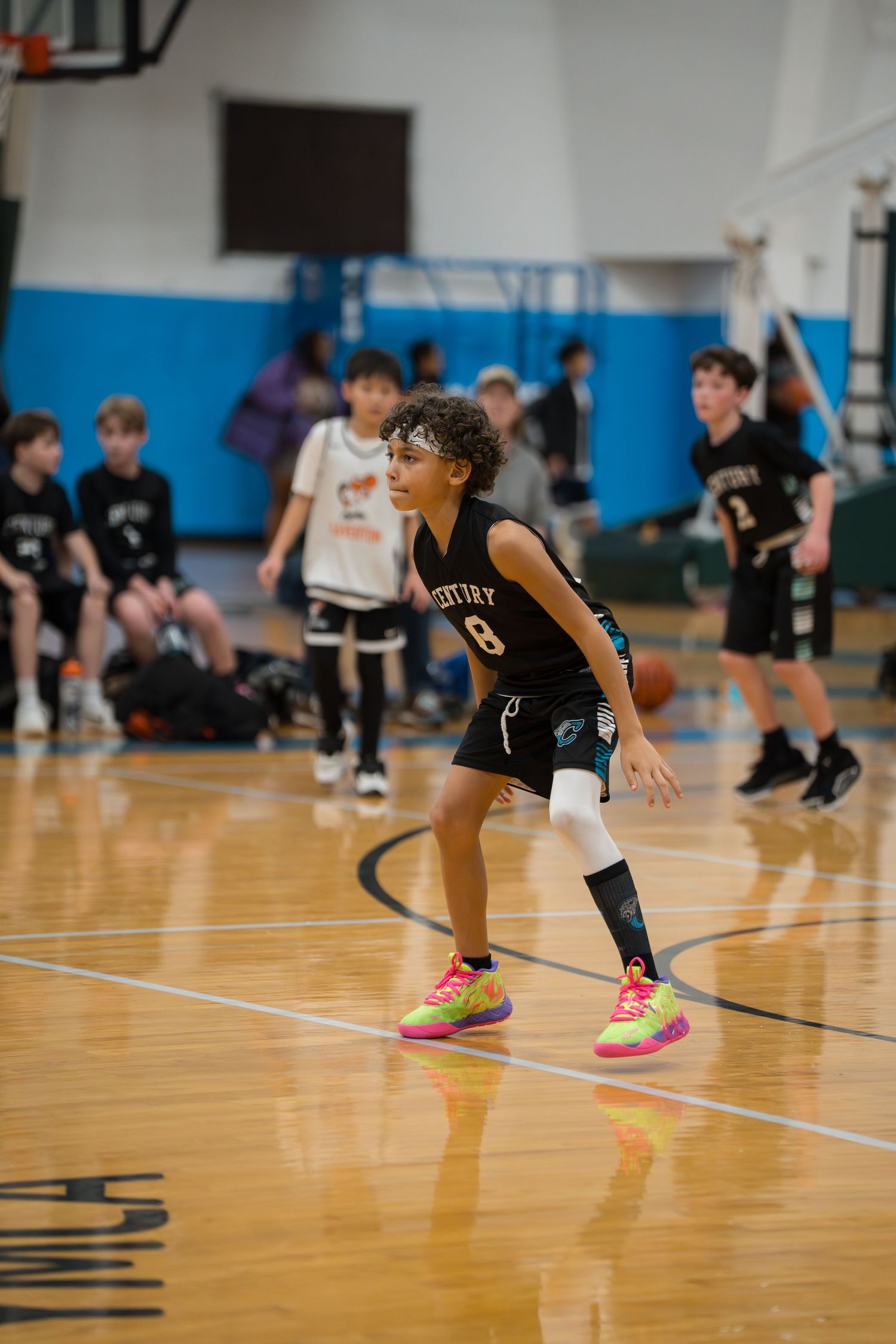 Basketball players in black uniforms practice defensive stance drills on a polished wooden gym court.