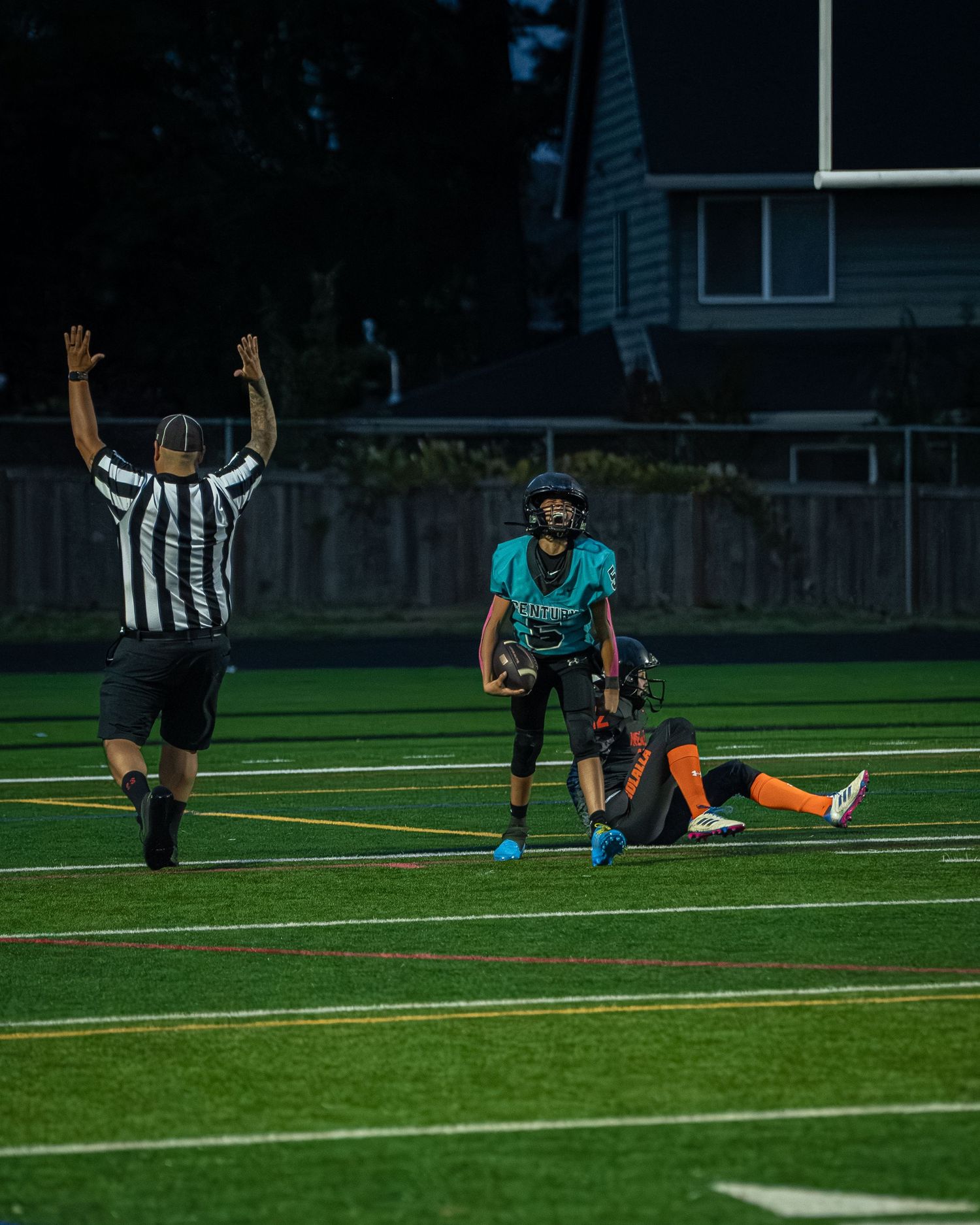 Football players and referees spread across the field during a nighttime practice session.