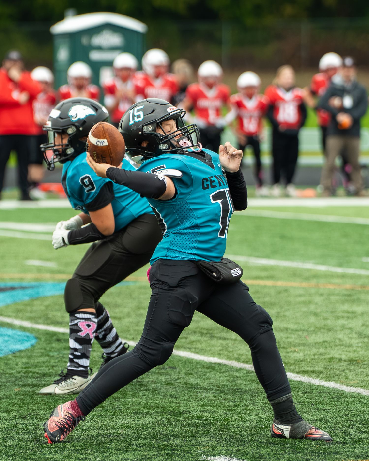 Football player in teal and black uniform stretches to catch a pass during a game on the field.