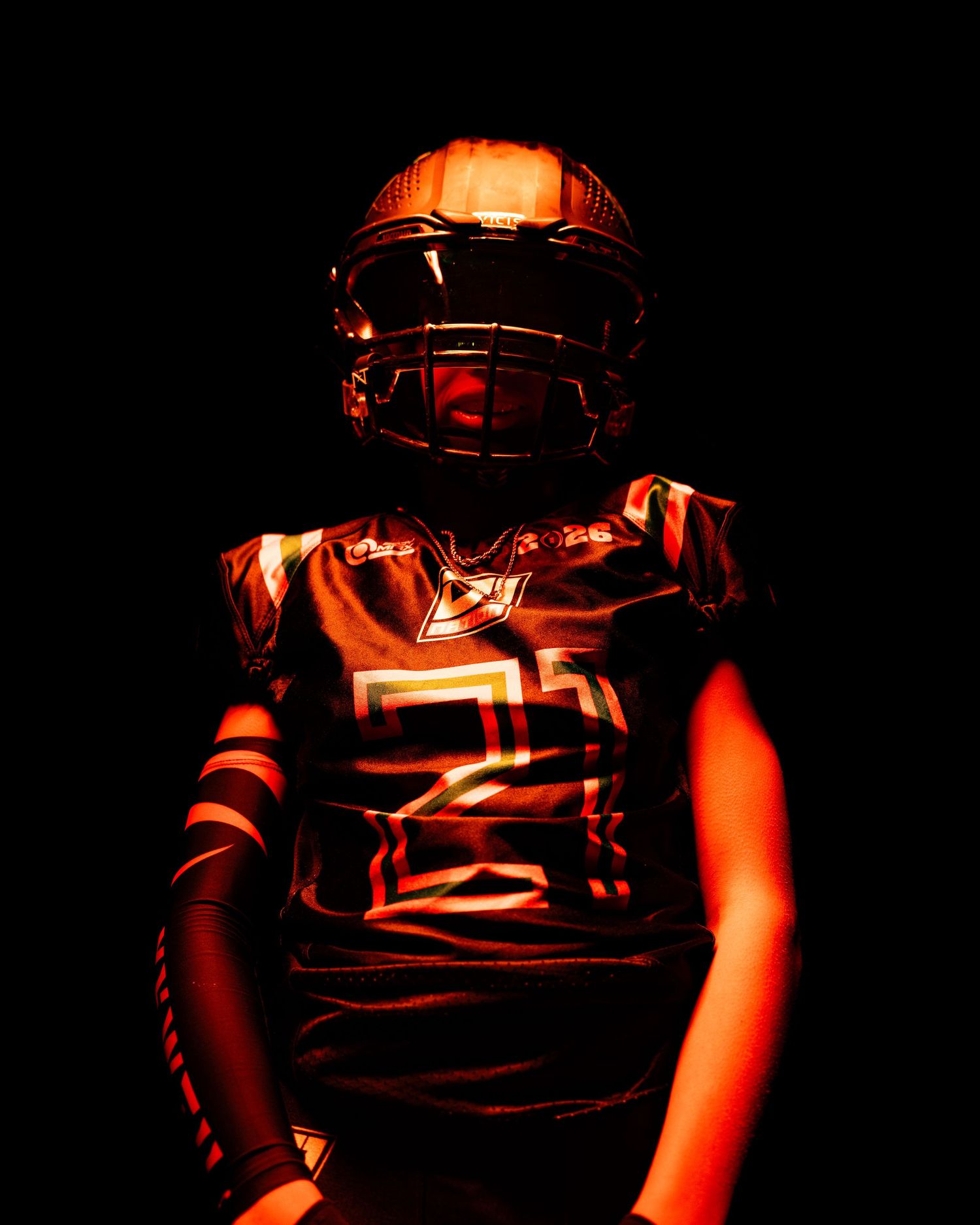 Dramatic low-key portrait of a football player in dark uniform illuminated by red lighting against black background.
