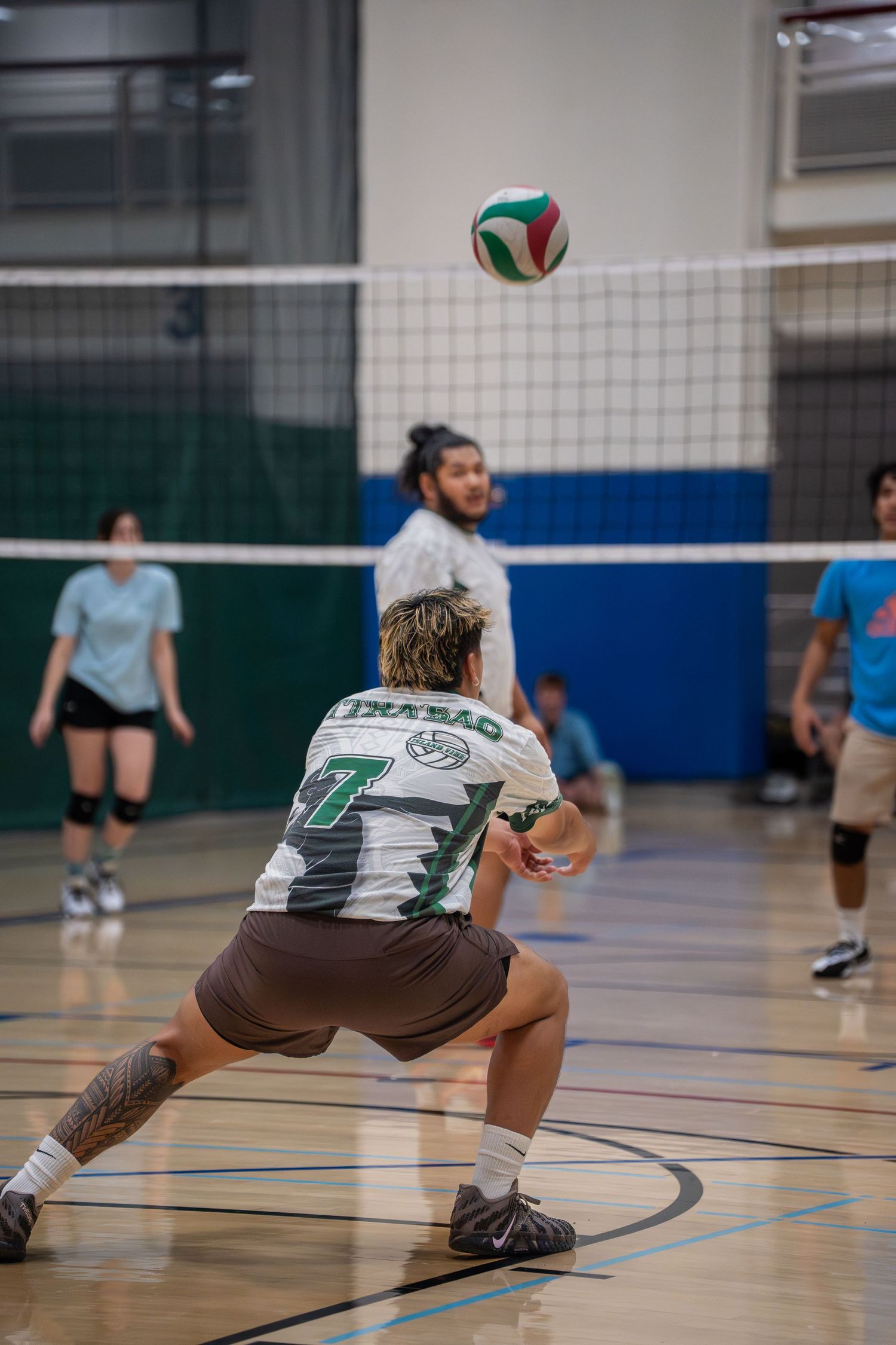 Volleyball player diving low to save a ball during an indoor match on a gymnasium court.