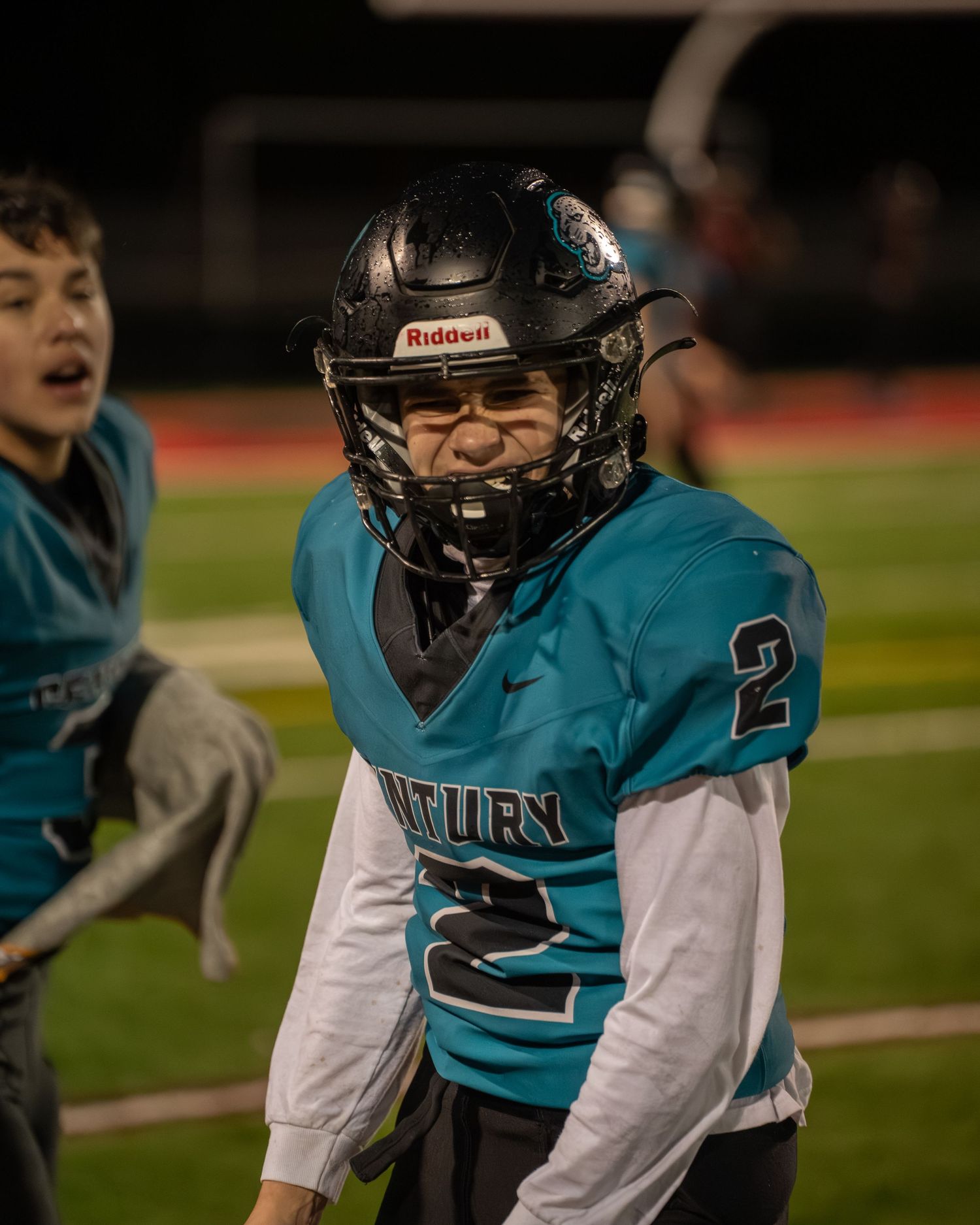 Football player in teal uniform preparing for snap during evening game.
