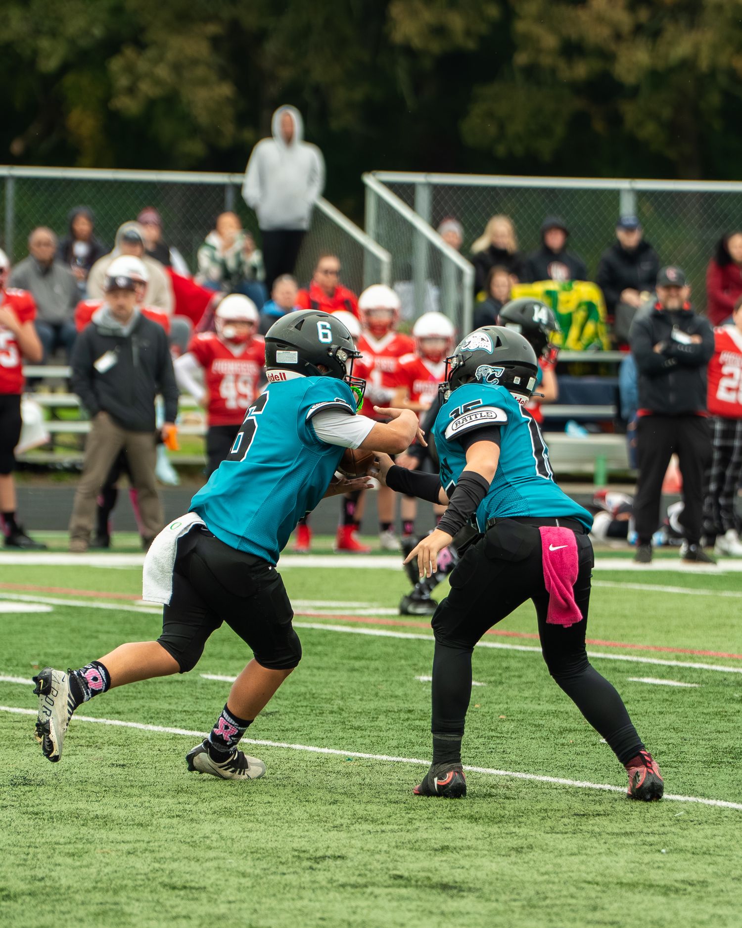 Two football players in teal jerseys practice blocking techniques on a turf field during a game.