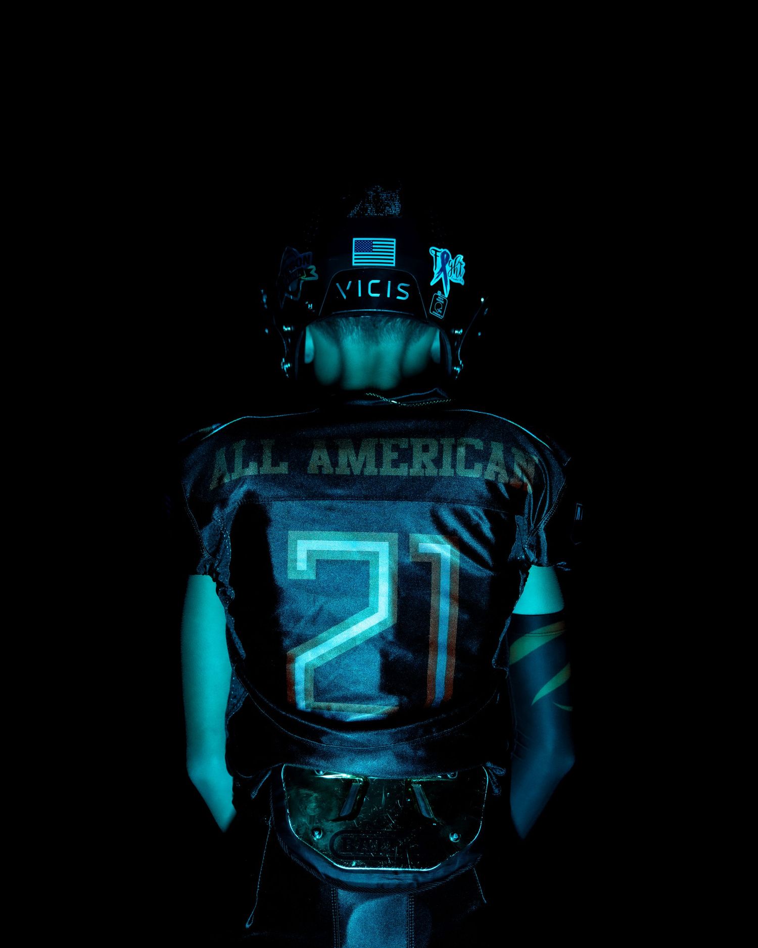 Football player wearing jersey number 21 illuminated in dramatic blue lighting against dark background.