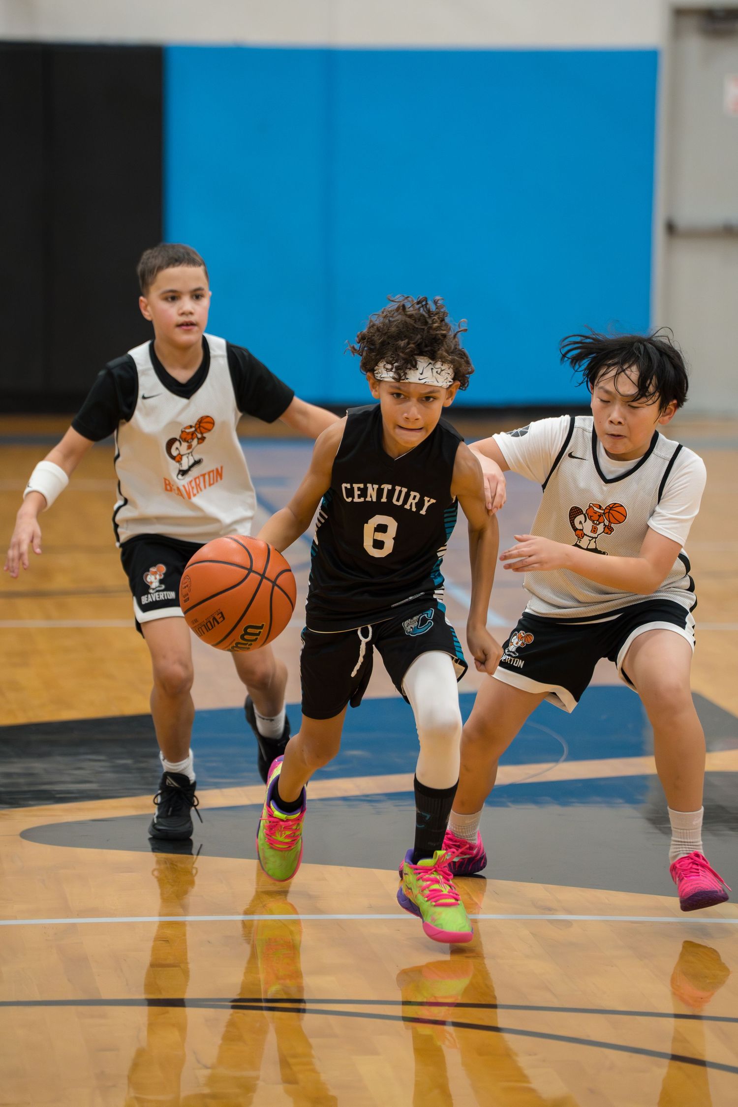 Basketball players in black and white uniforms crouch low in defensive positions during an indoor game.