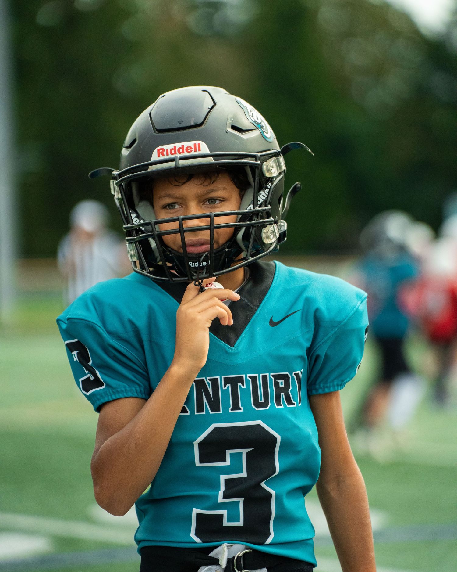 Player in teal jersey number 3 adjusts football helmet during game.
