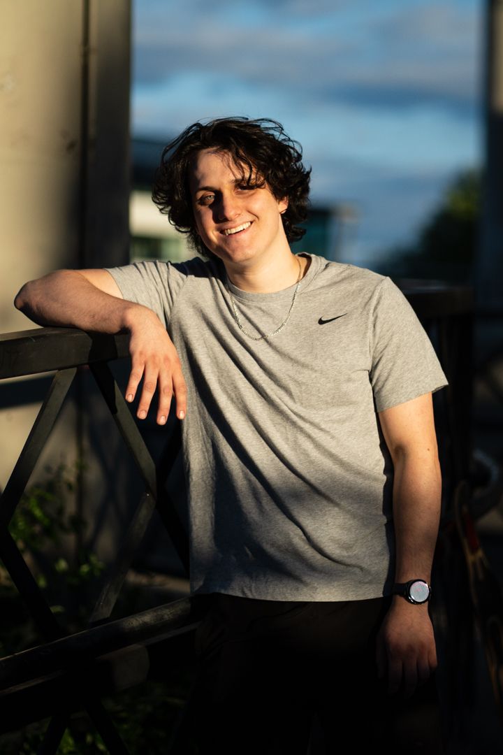 Person in grey t-shirt sitting outdoors during golden hour with natural lighting.