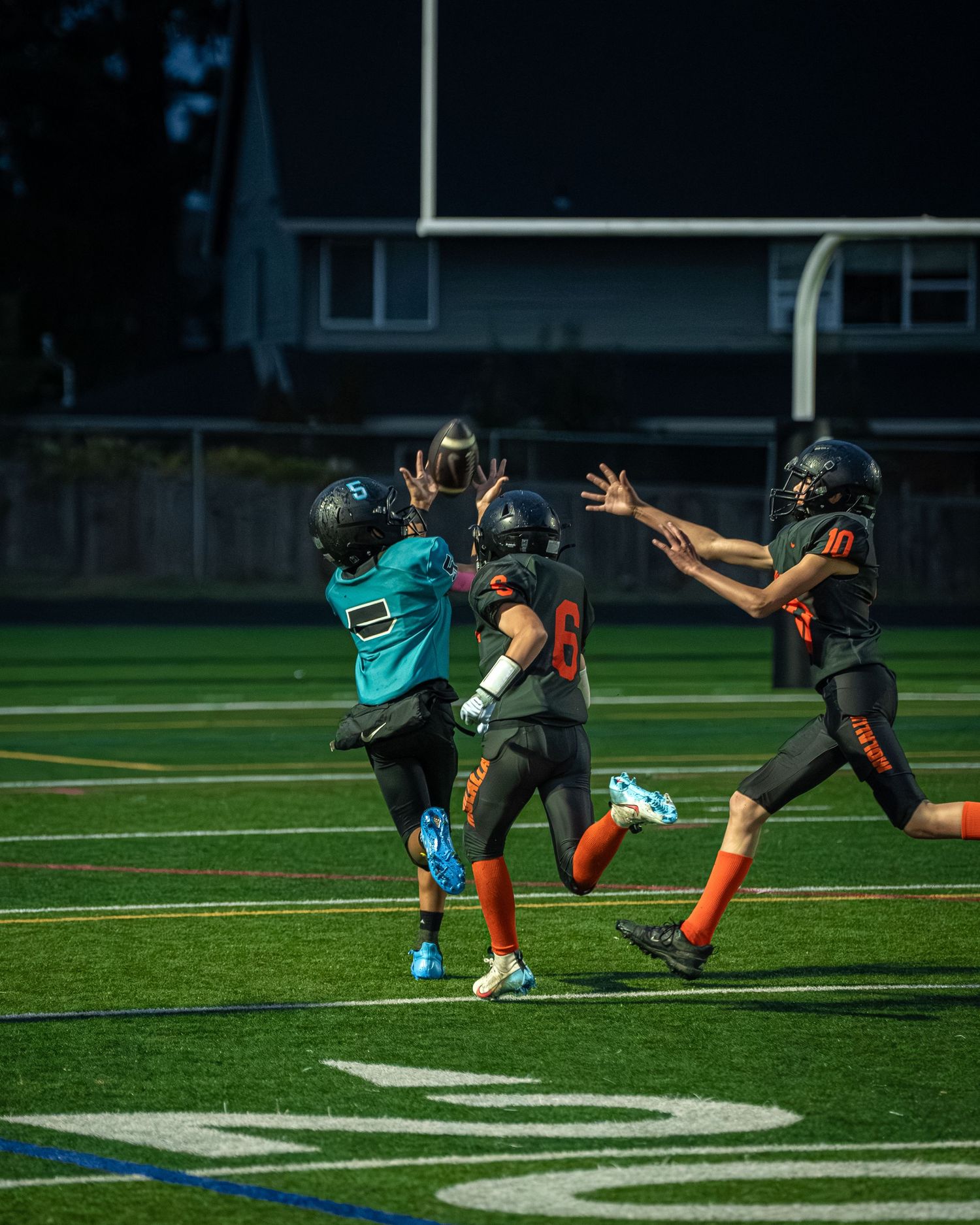 Football players in teal and orange uniforms engaged in a defensive play on the field.