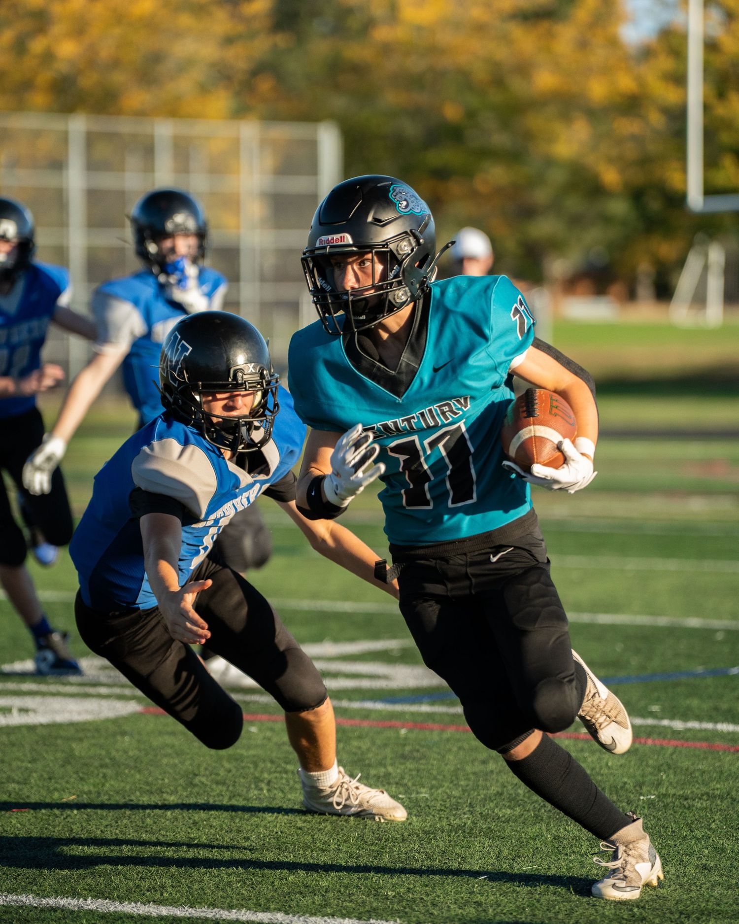 Football players in teal jerseys execute diving drills during practice session.