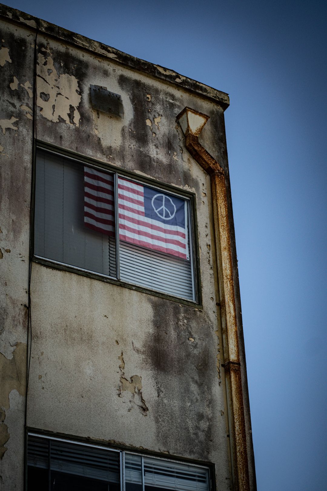 American flag with peace symbol displayed in window of weathered building.