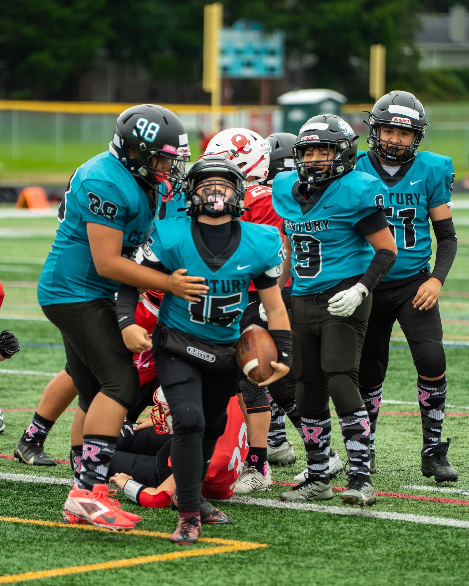 Football teammates in teal jerseys celebrate after a successful play.