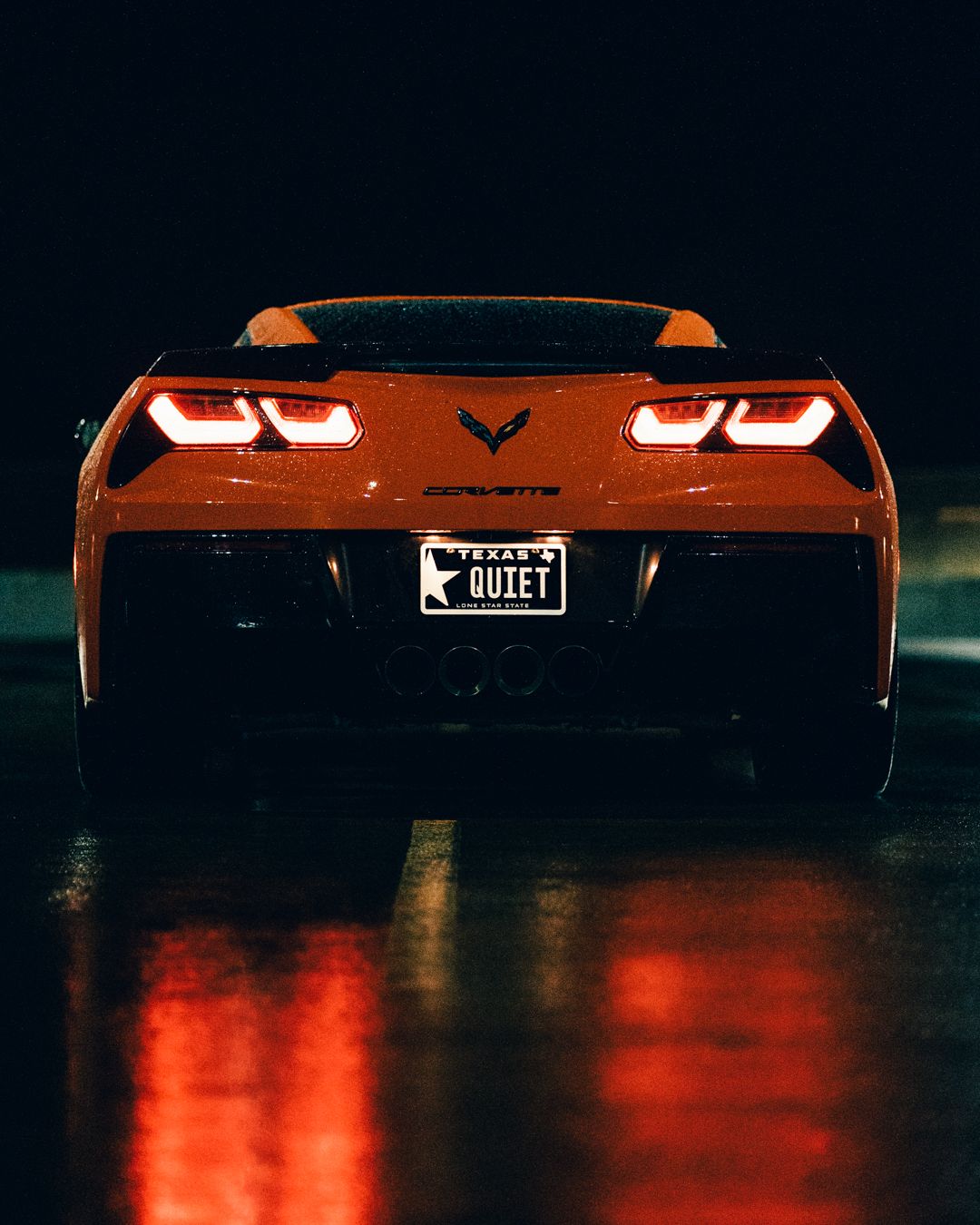 Low profile shot of orange Corvette taillights glowing in dark parking structure.