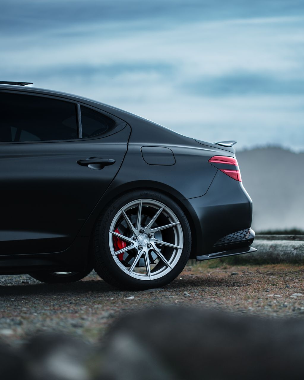 Close-up view of a black luxury car's rear wheel with silver alloy rims and red brake calipers.