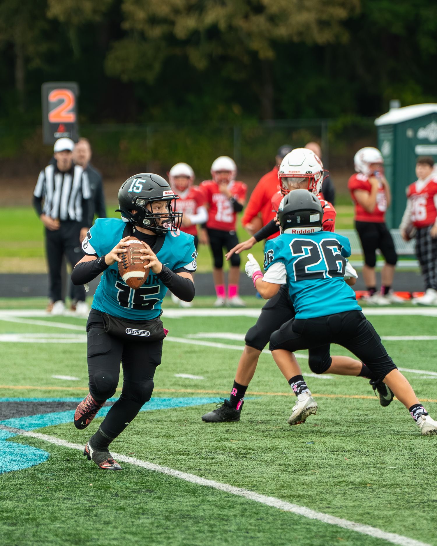 A quarterback in teal looks to pass while teammate provides blocking protection.