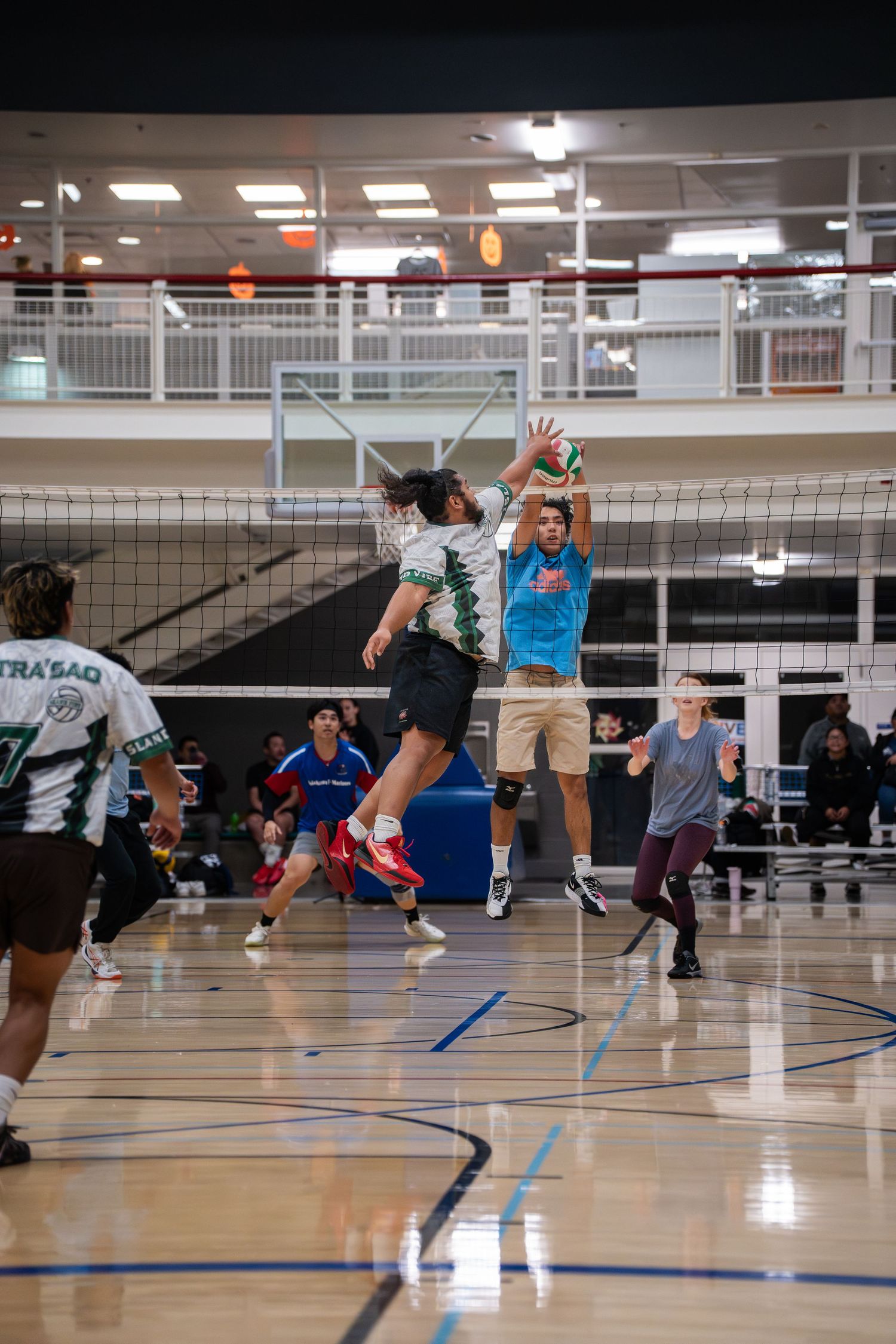 Players jumping at the net during a competitive indoor volleyball game.